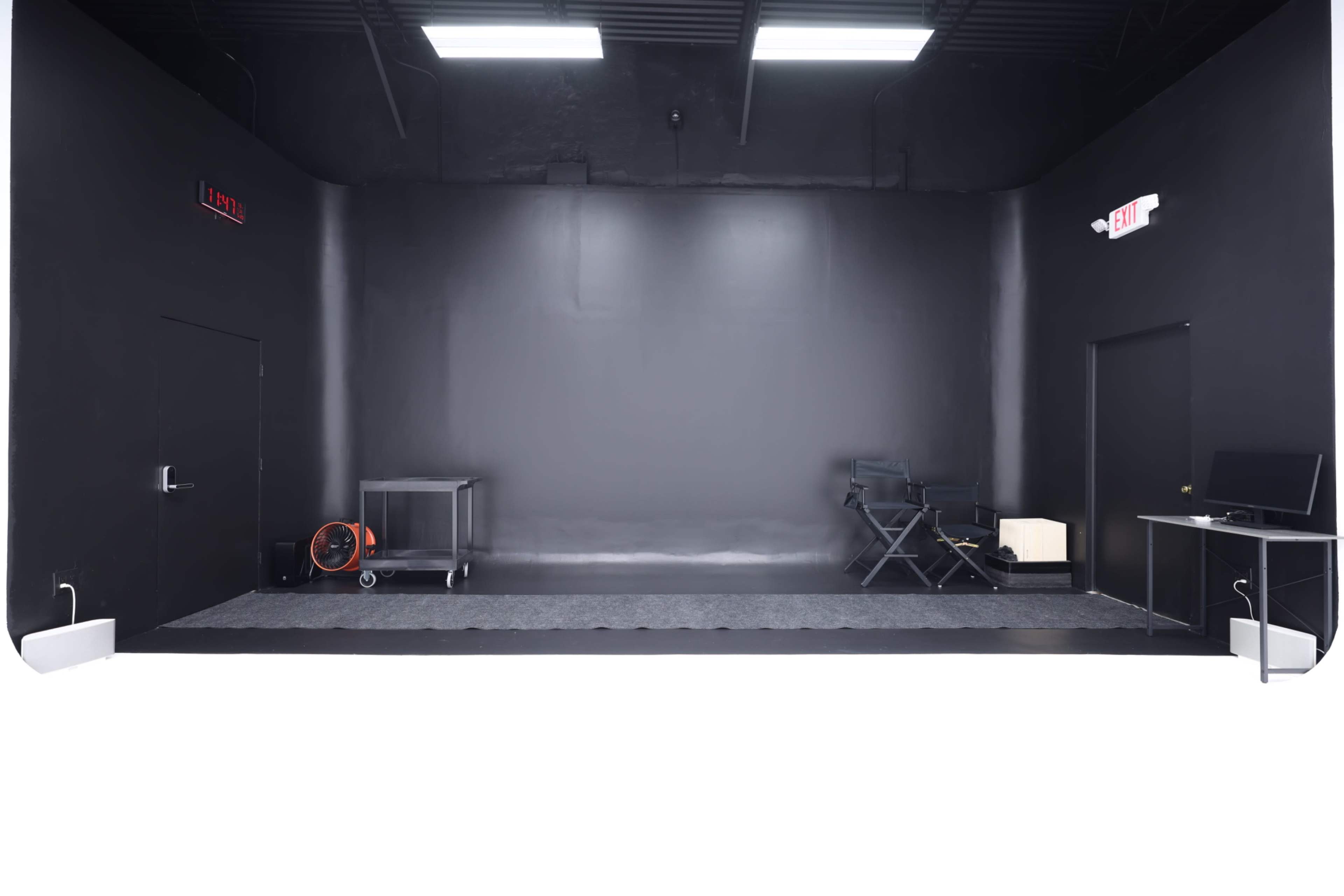 The image shows an empty black room featuring two doors, a cart on wheels, a director's chair, and a monitor on a table.