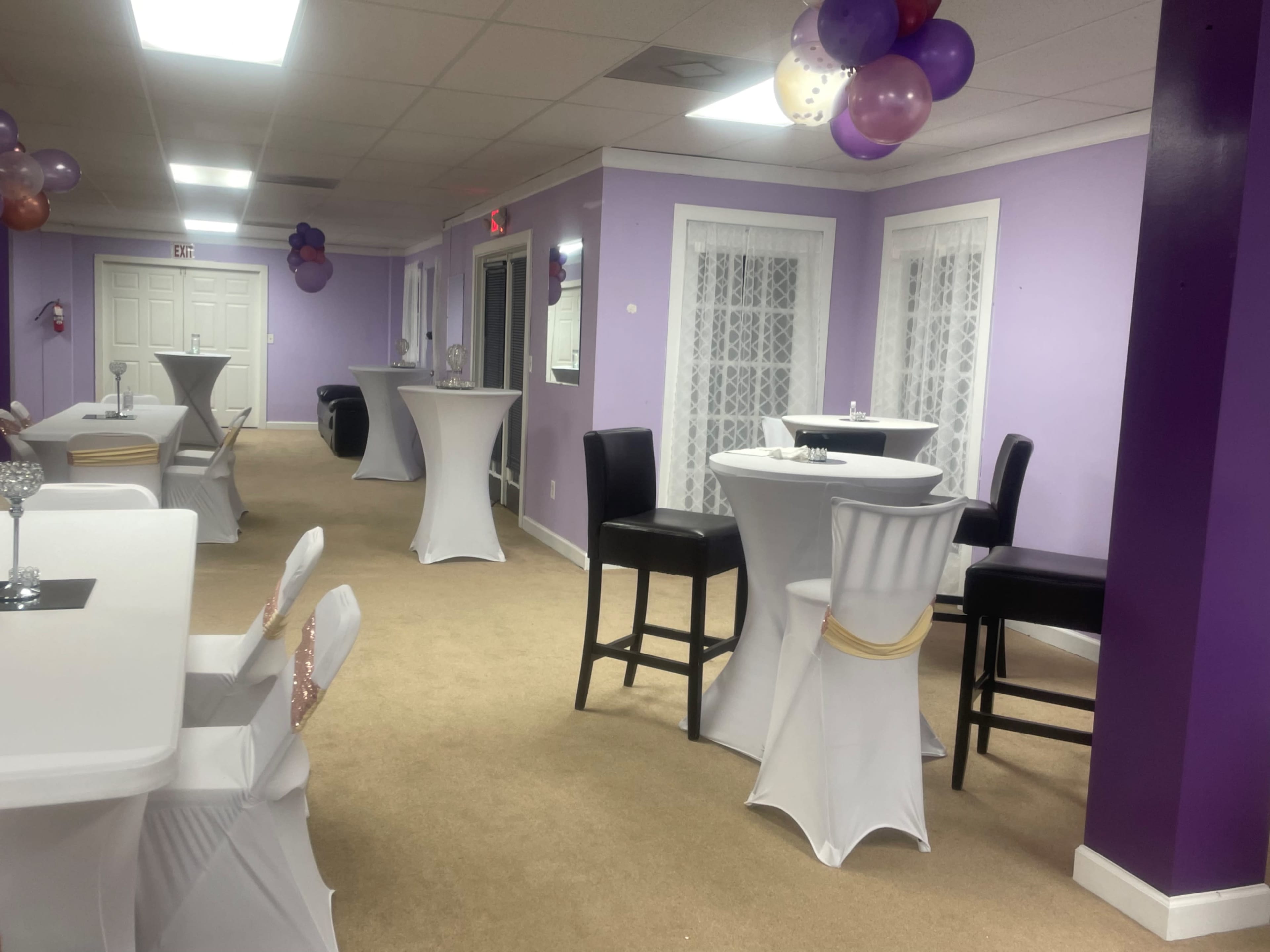A banquet hall with white tables and chairs, purple walls, and decorative balloons.