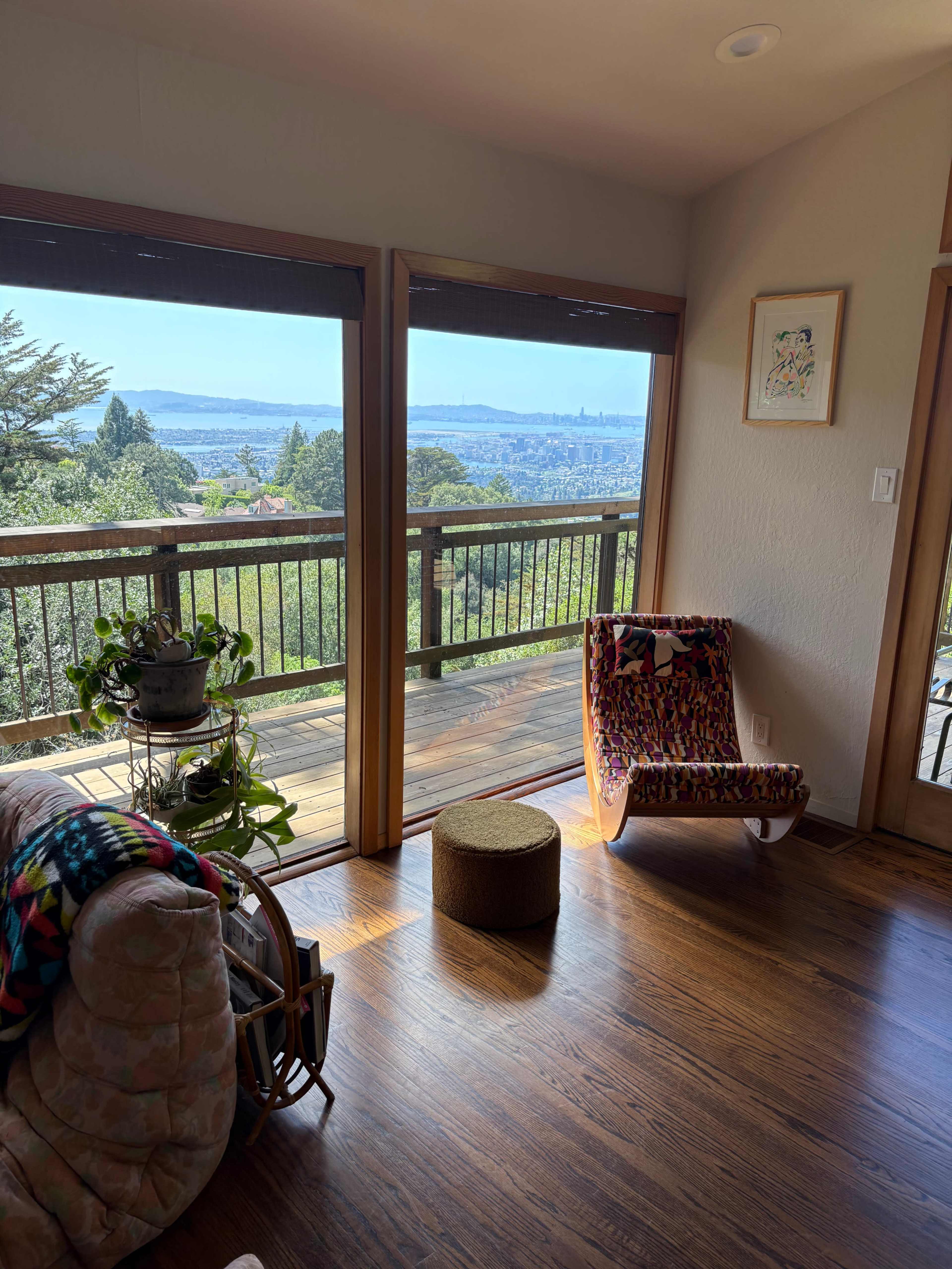 A cozy living room features large glass doors opening to a scenic view of the landscape and city beyond, with a colorful chair and plants nearby.