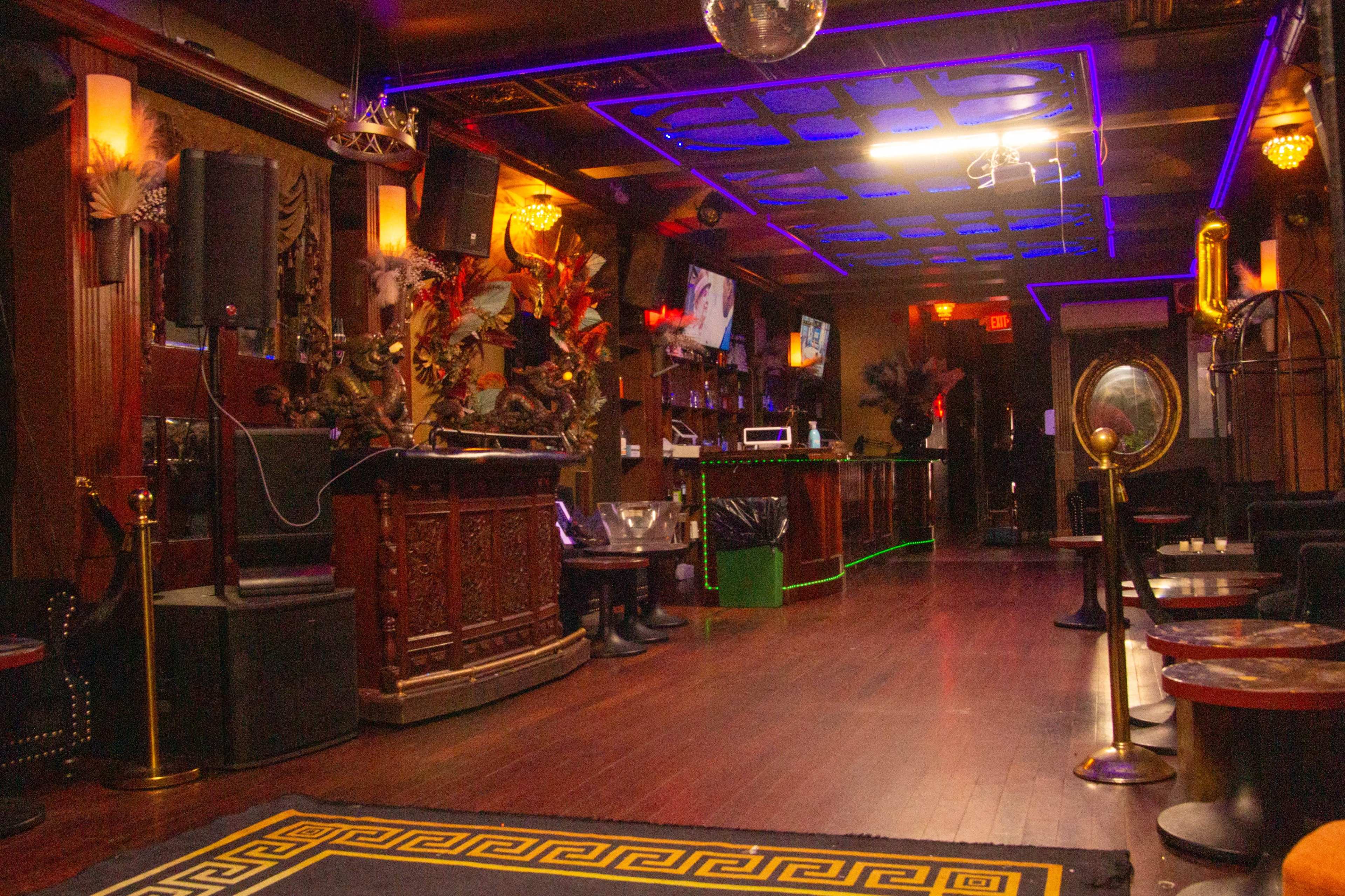 A dimly lit bar with ornate decor, a wooden bar counter, and neon blue lighting illuminating the ceiling and walls.