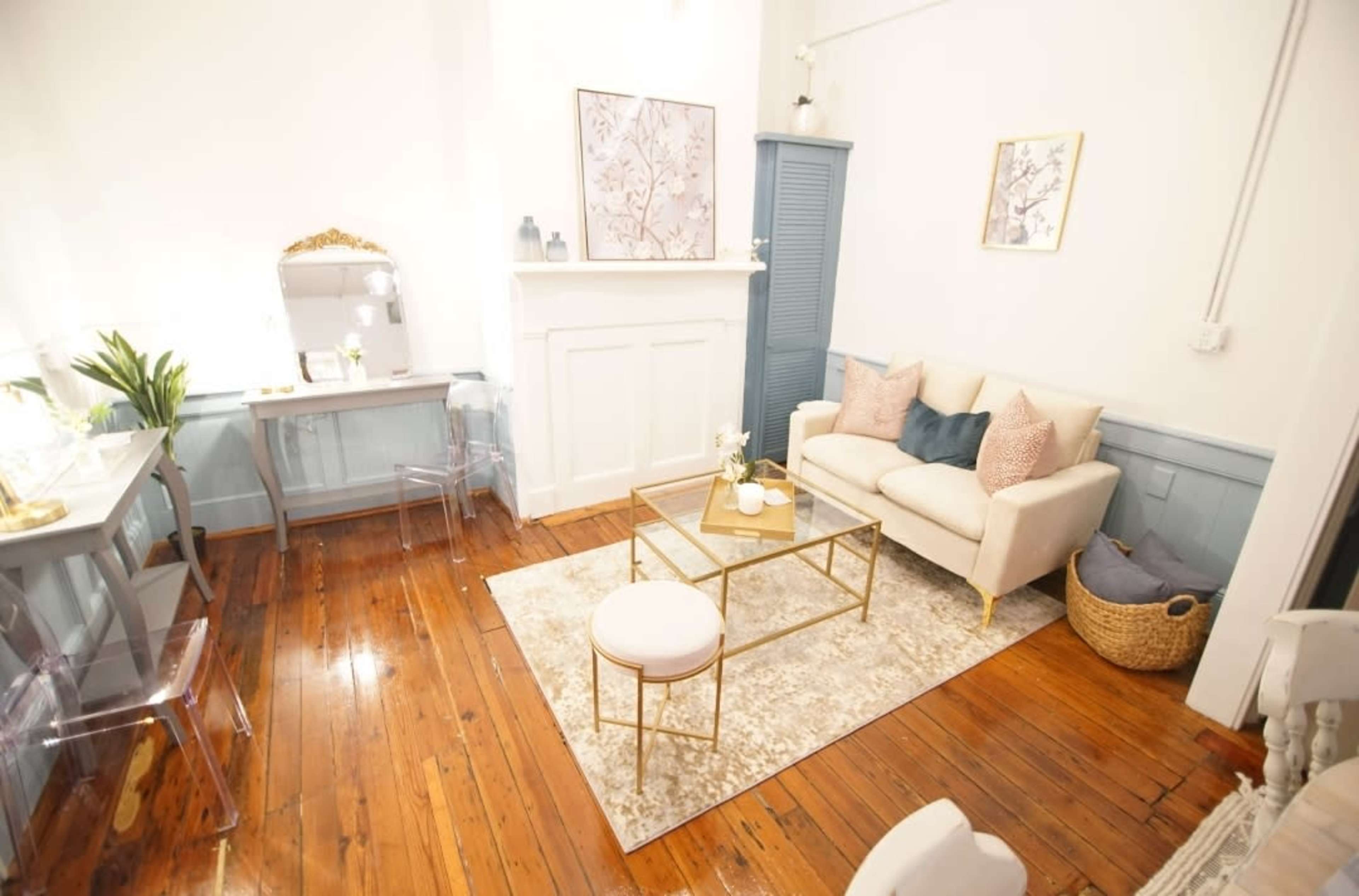 A well-decorated living room featuring a beige sofa, a glass coffee table, a woven basket, and a small desk near a fireplace.