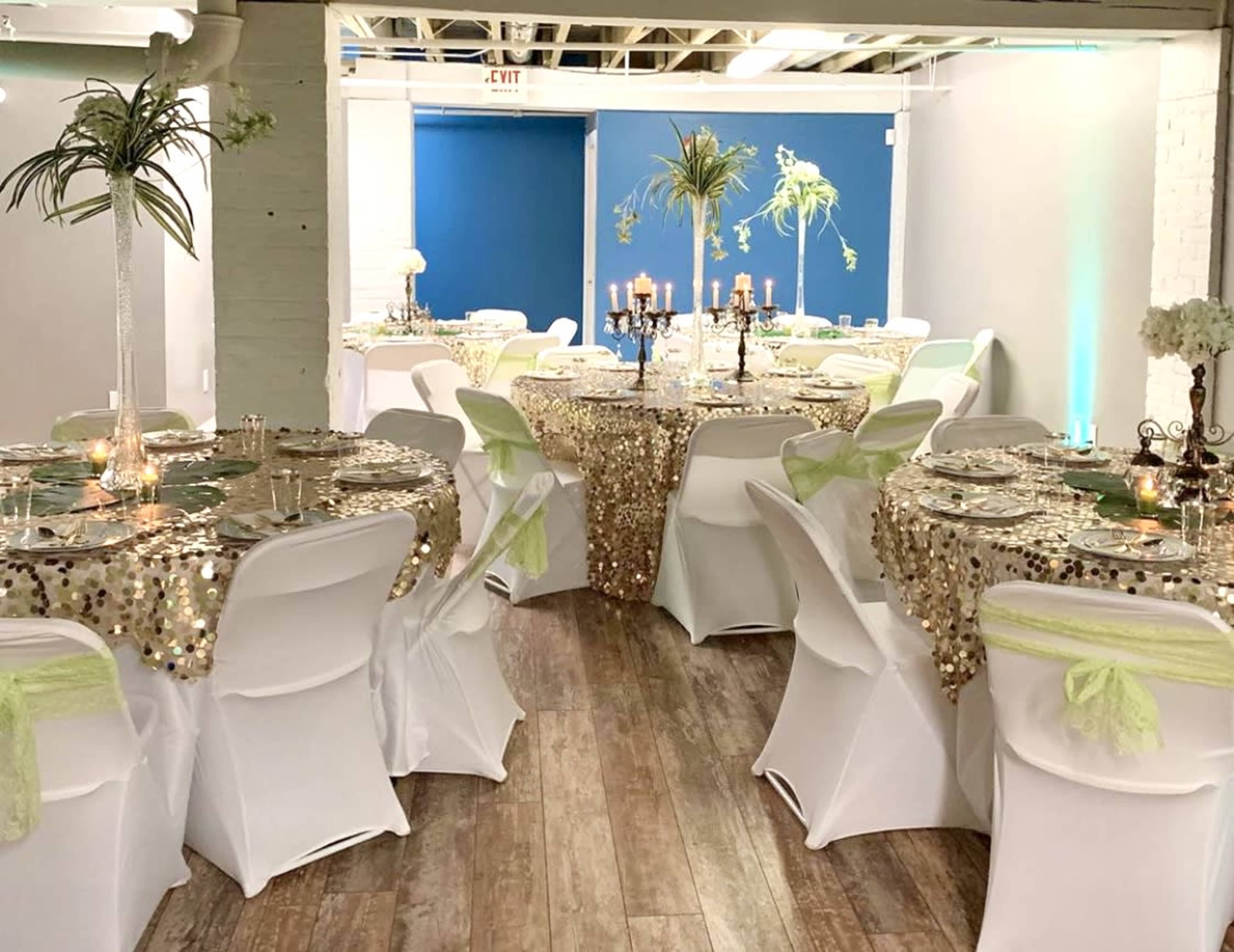 The image shows a decorated event space with elegantly arranged tables covered in sequin tablecloths, adorned with candles and centerpieces.