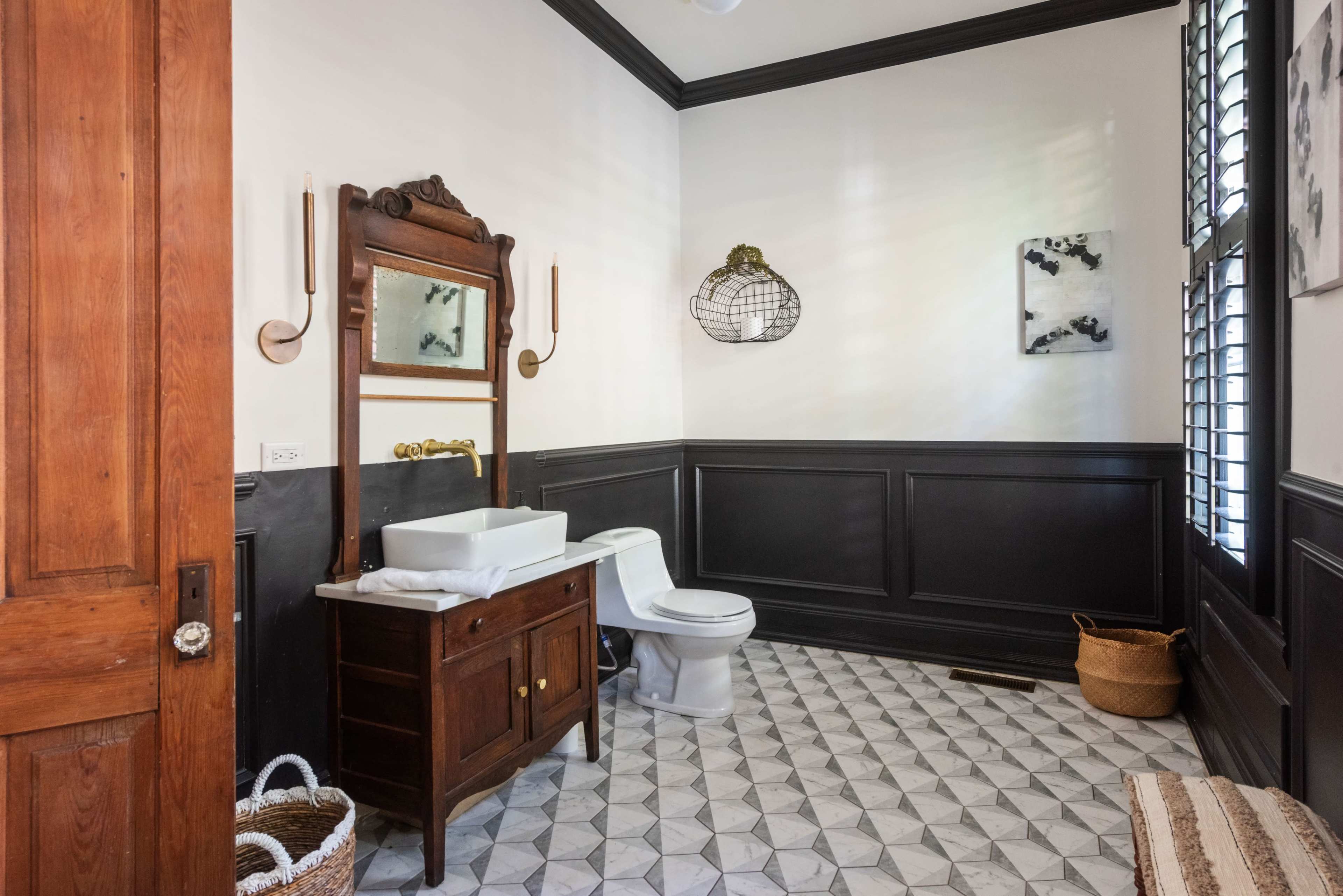 The bathroom features a wooden vanity with a sink, a toilet, and patterned tile flooring, complemented by wall sconces and a wall-mounted light fixture.