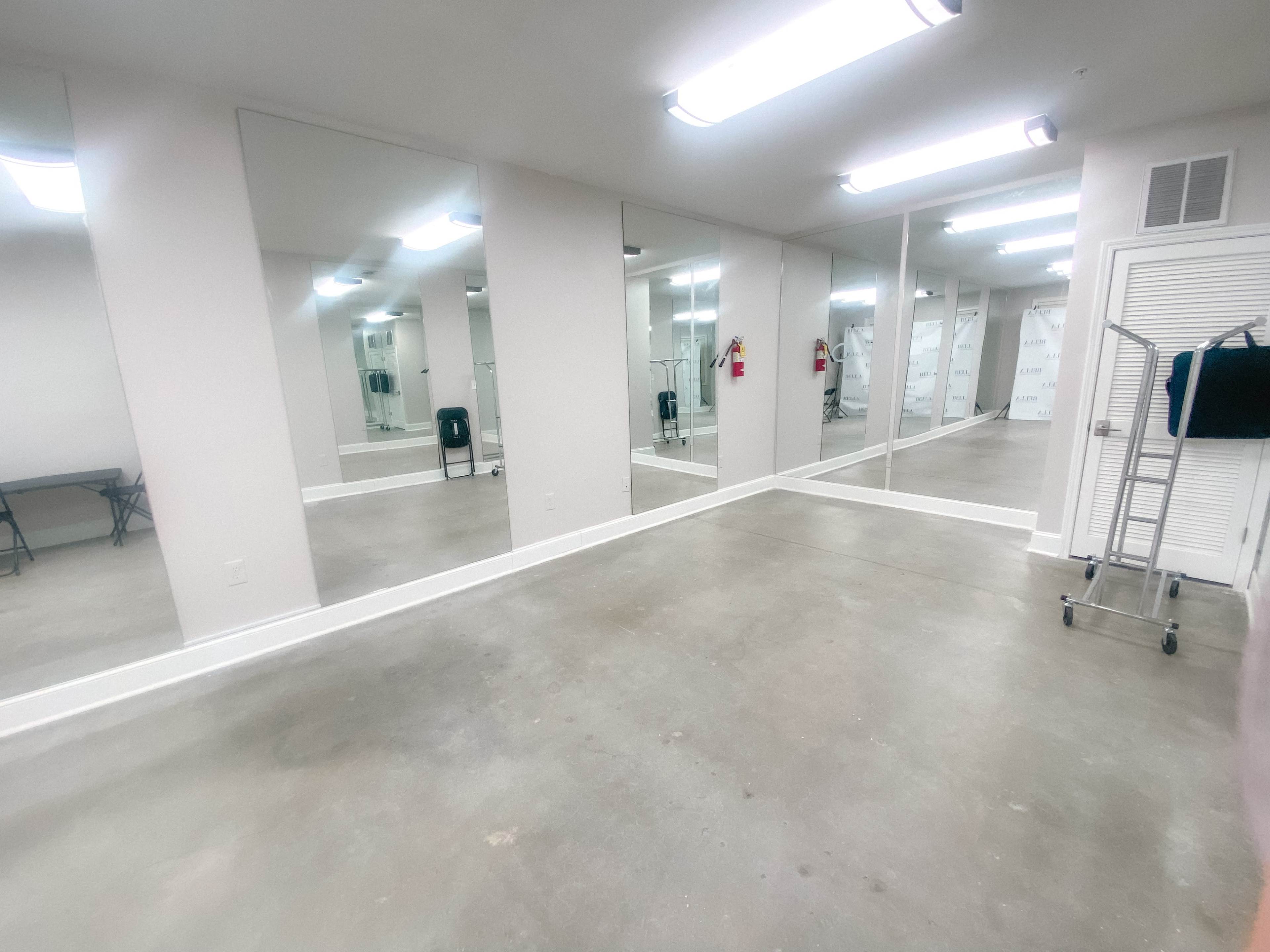 A spacious, well-lit room with multiple mirrors along one wall and industrial-style lighting.