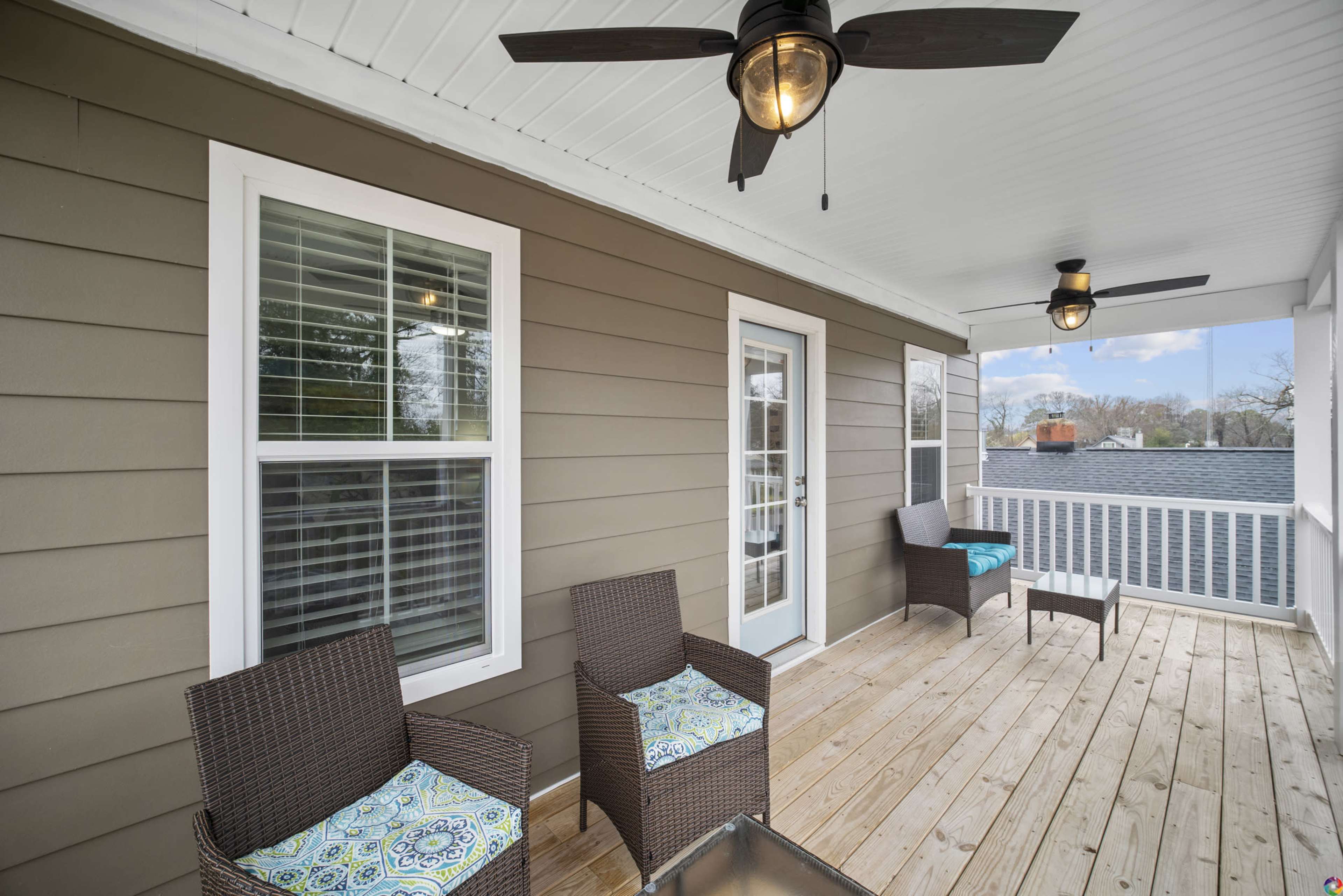 A porch with two wicker chairs and a small table, featuring a ceiling fan and large windows along the walls.