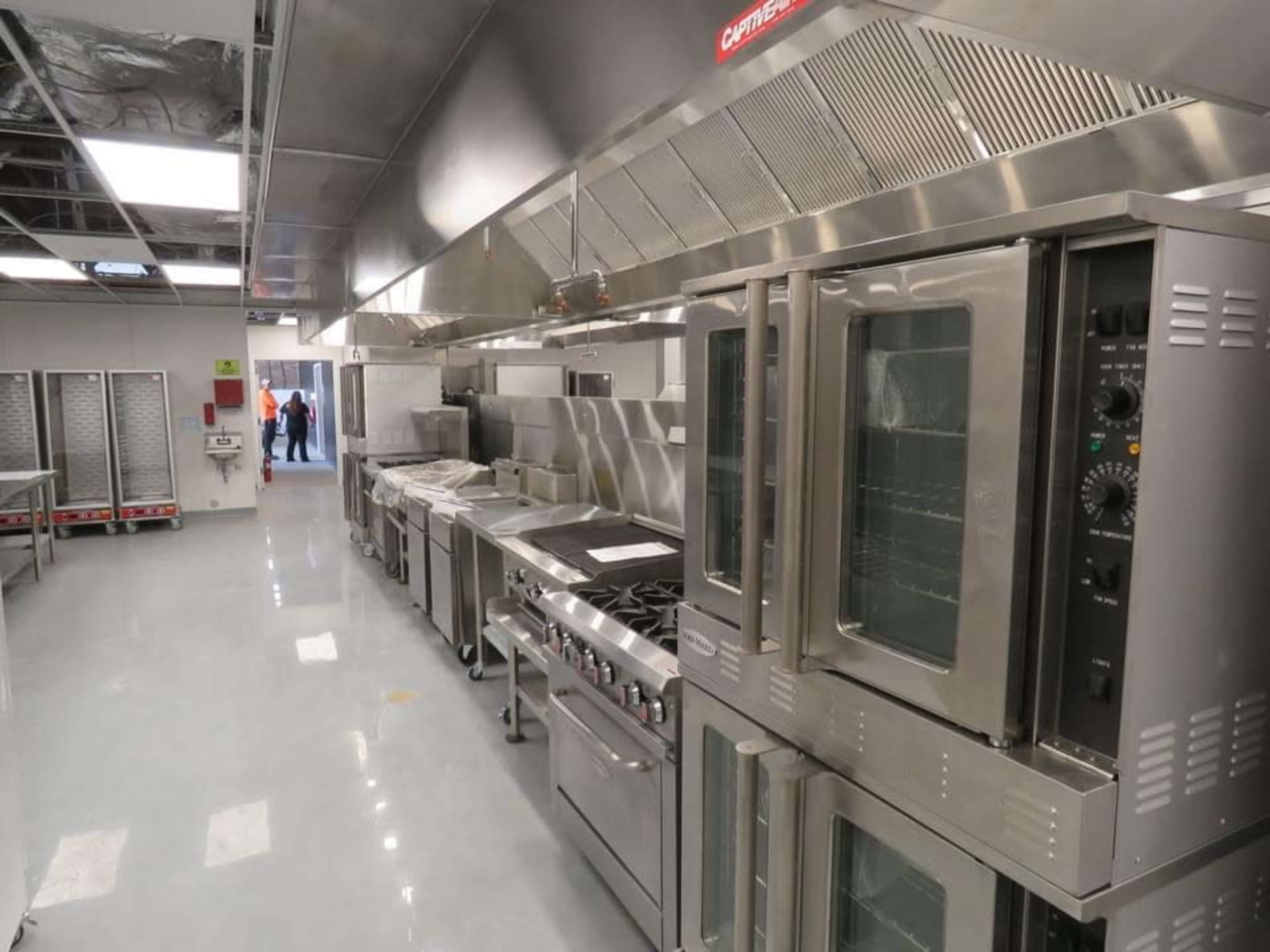 A commercial kitchen equipped with stainless steel appliances, including ovens and cooktops, and a door leading to another area.