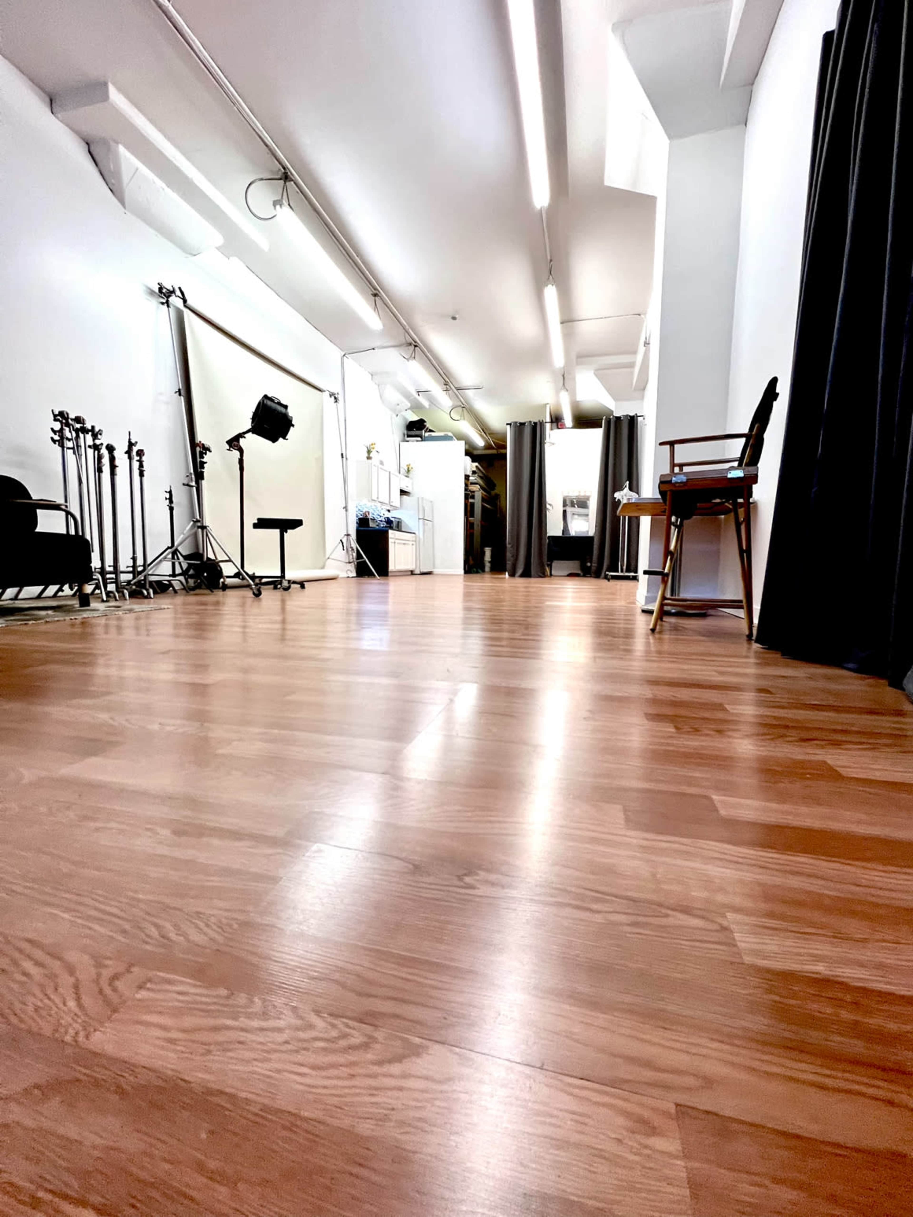 The image shows a spacious studio with a wooden floor, soft lighting, and various photography equipment in the background.