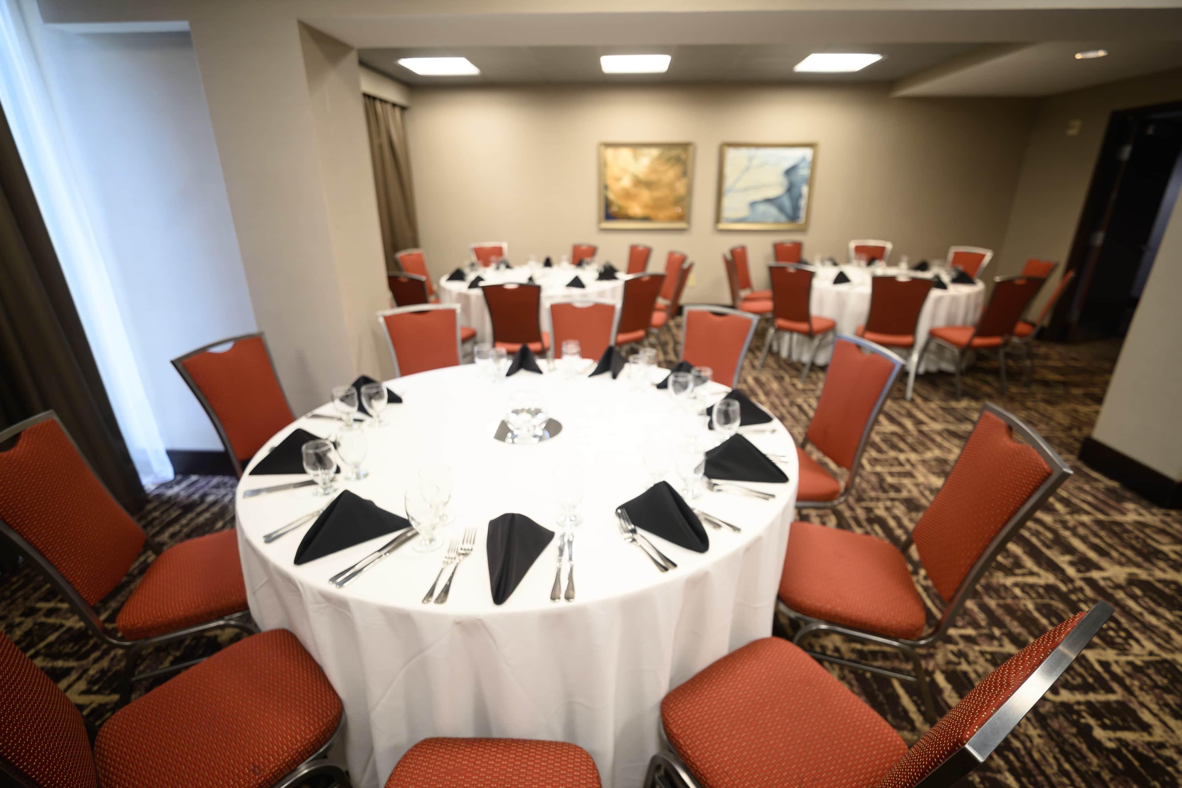 The image shows a set of round tables covered with white tablecloths and red chairs arranged in a dining area, ready for a formal event.