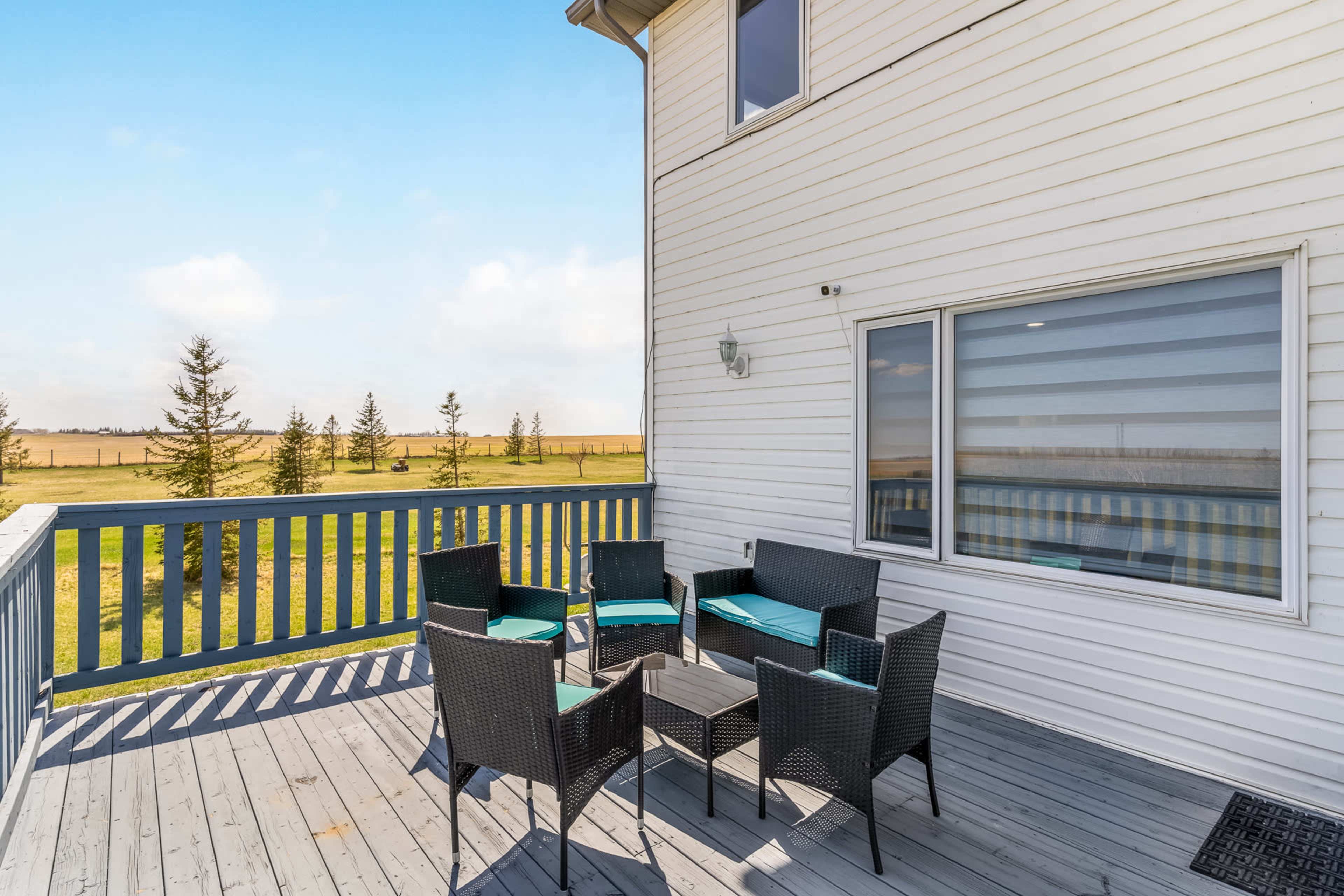 A patio area features a set of wicker chairs and a table, with a view of an open field and a clear sky in the background.