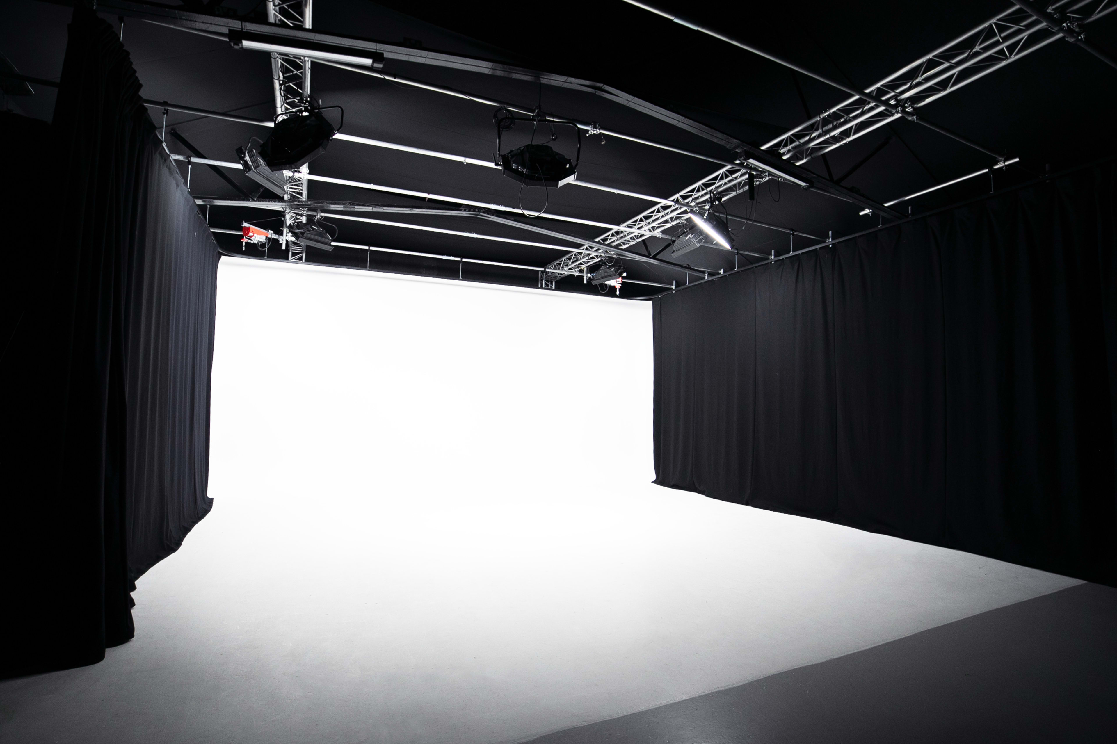 The image shows a spacious photography studio with black curtains and a bright white backdrop.