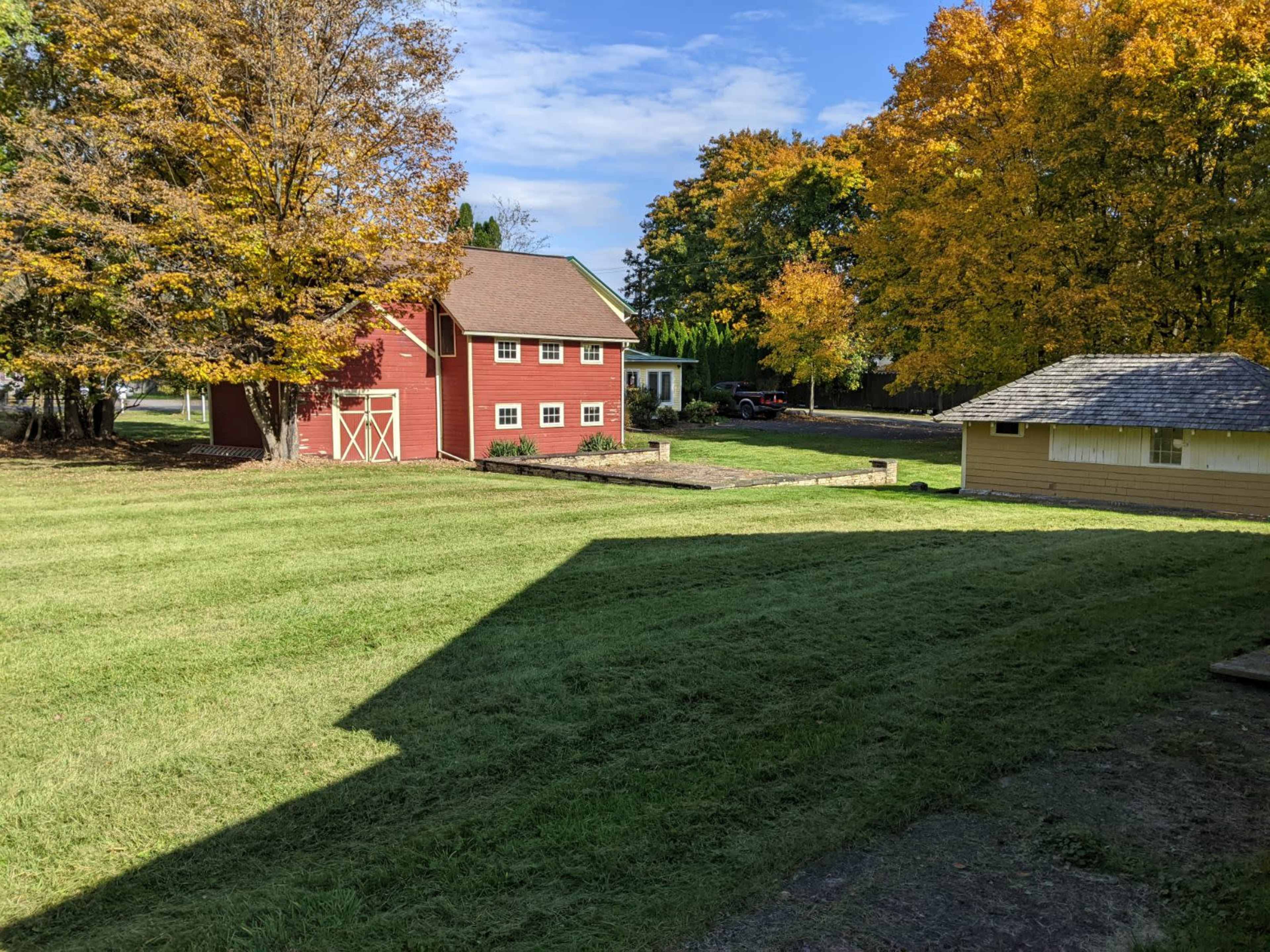 A red barn stands in a grassy area surrounded by trees with autumn foliage.