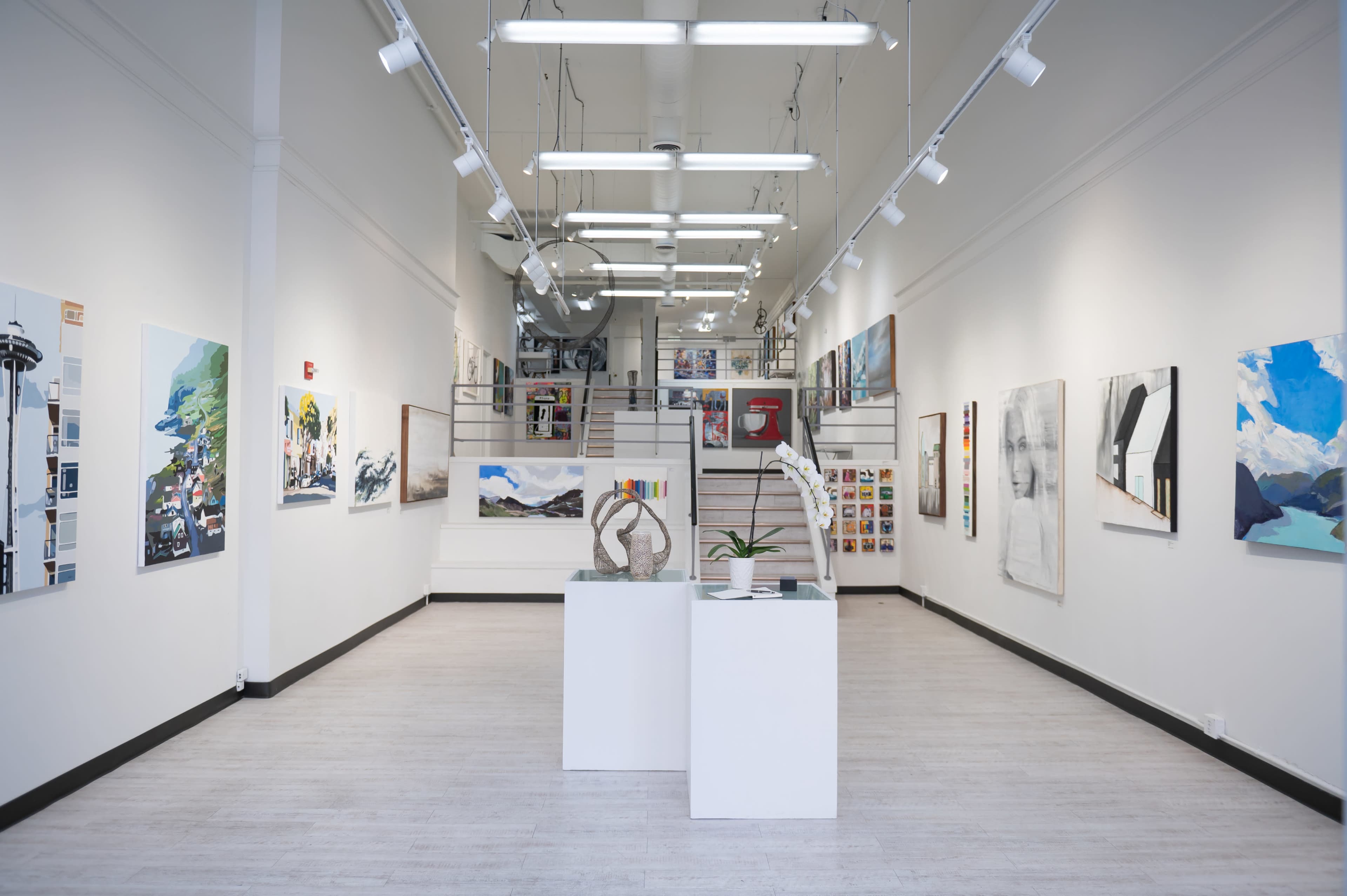 A modern art gallery featuring various paintings and sculptures displayed on the walls and a central pedestal.