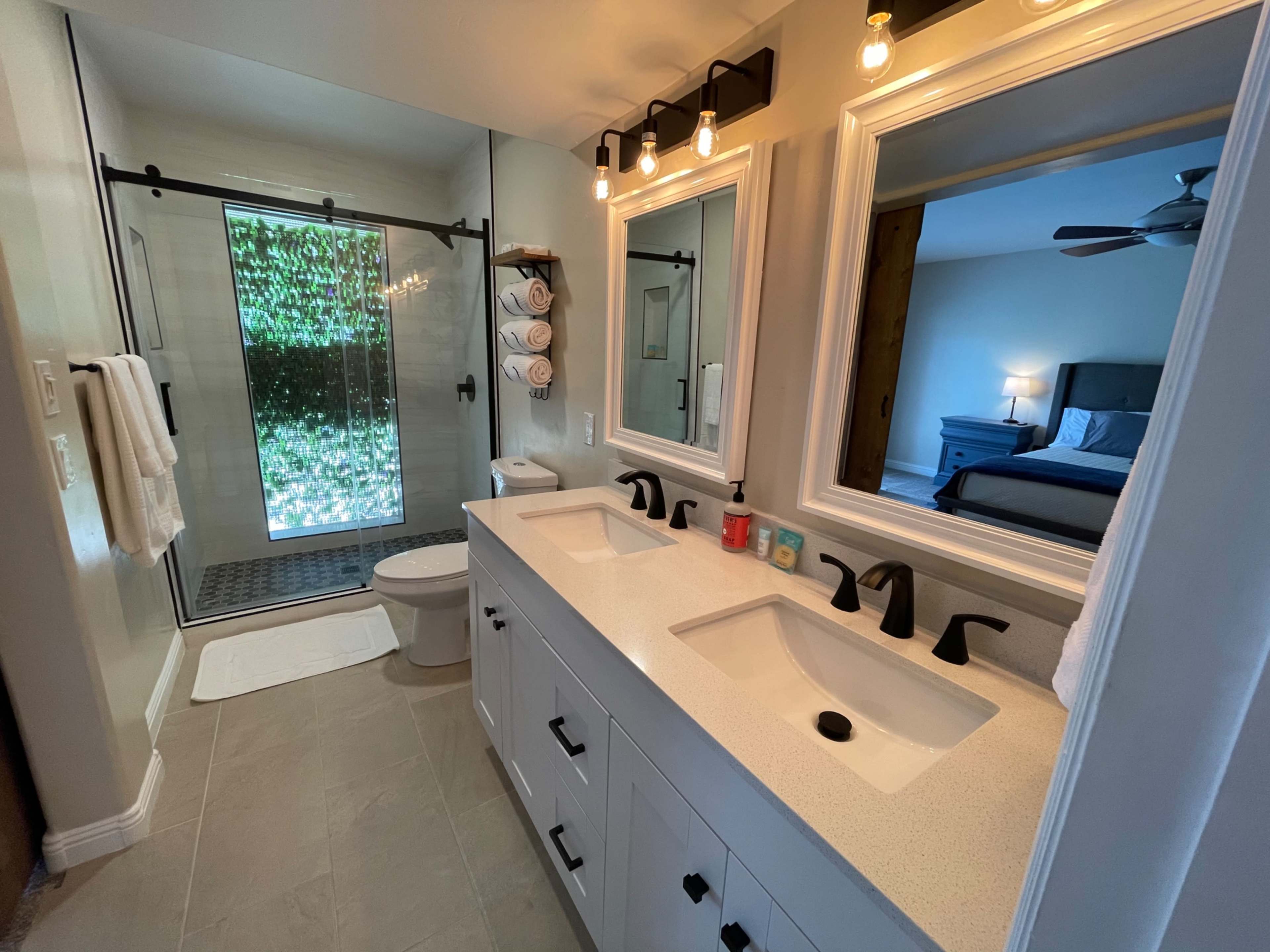 A modern bathroom with dual sinks, a glass shower, and a toilet, alongside mirrors and neatly arranged towels.