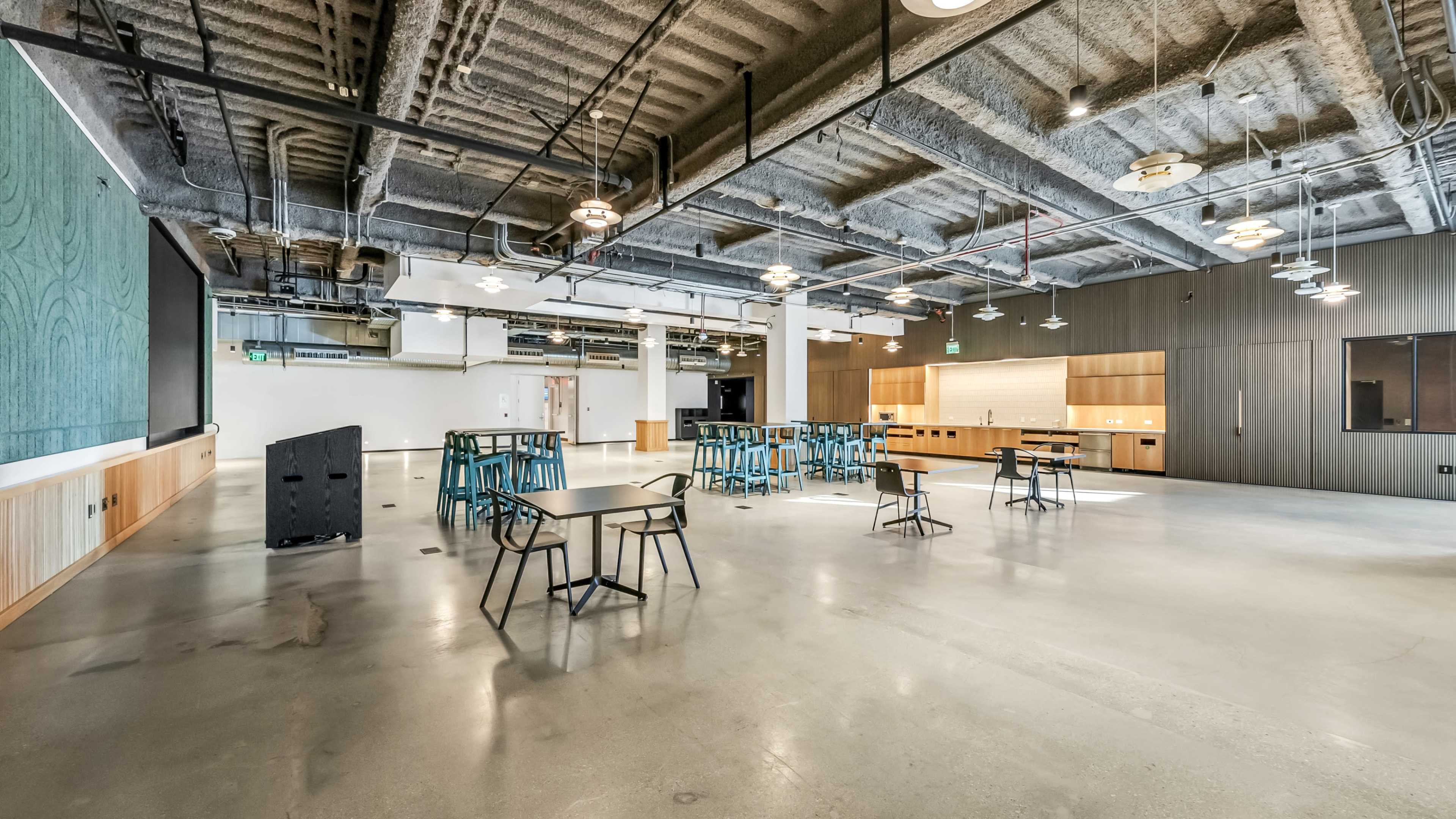 A spacious, modern interior of an empty office or communal area with concrete flooring and exposed ceiling structures.