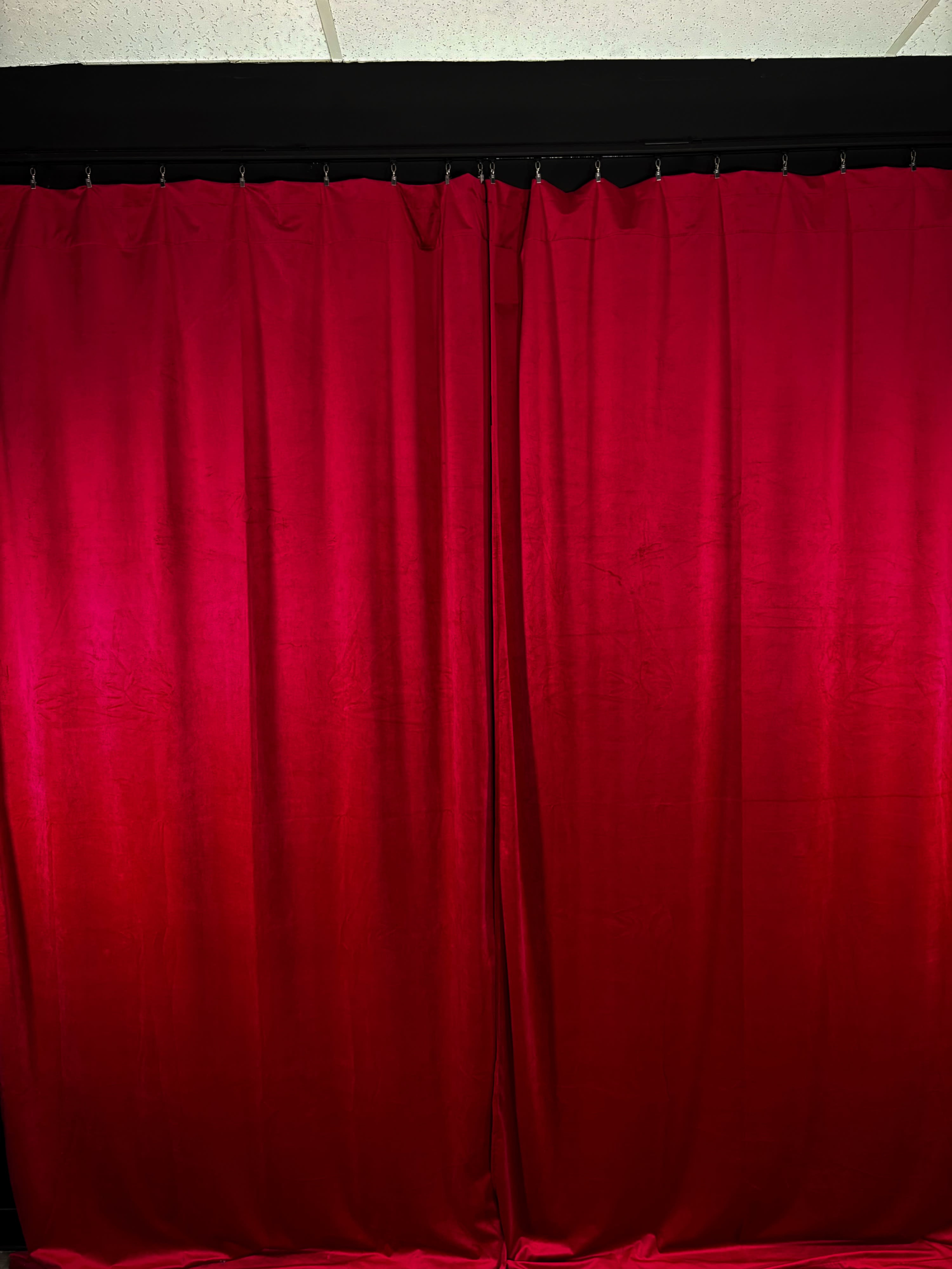 The image shows a pair of red velvet curtains hanging in front of a black backdrop.