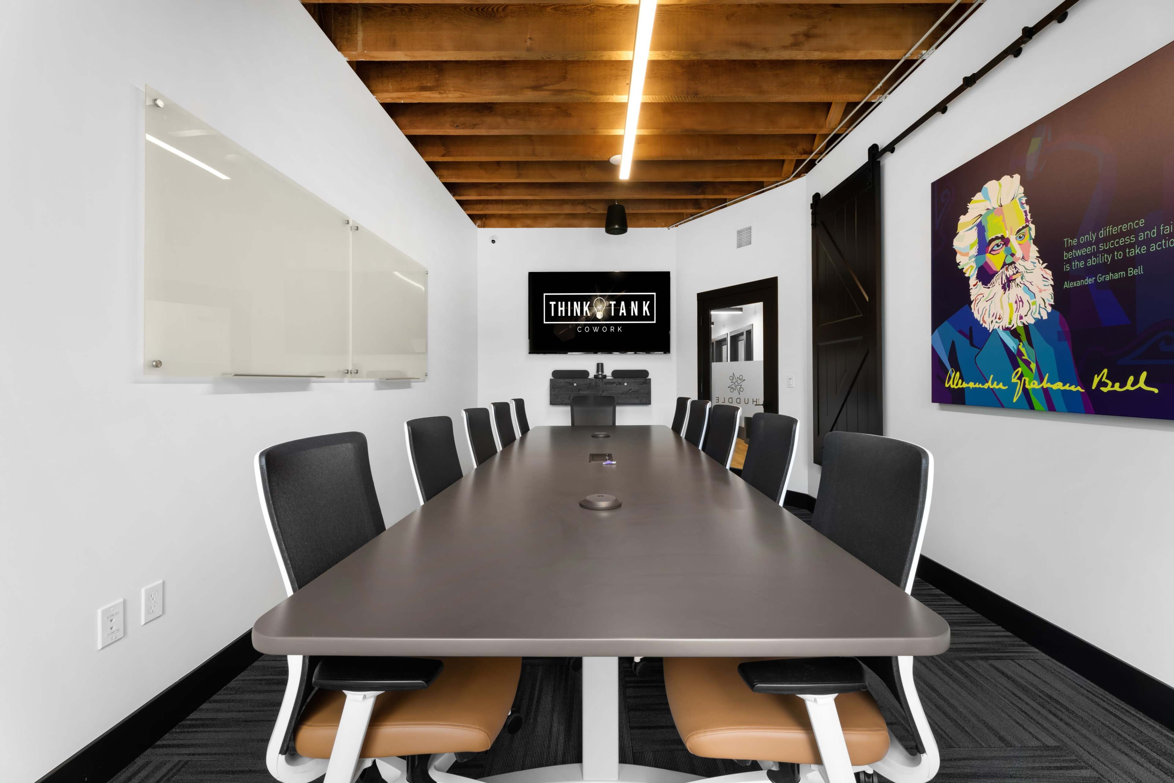 A modern conference room features a long table surrounded by ergonomic chairs, with a large screen and artwork on the walls.