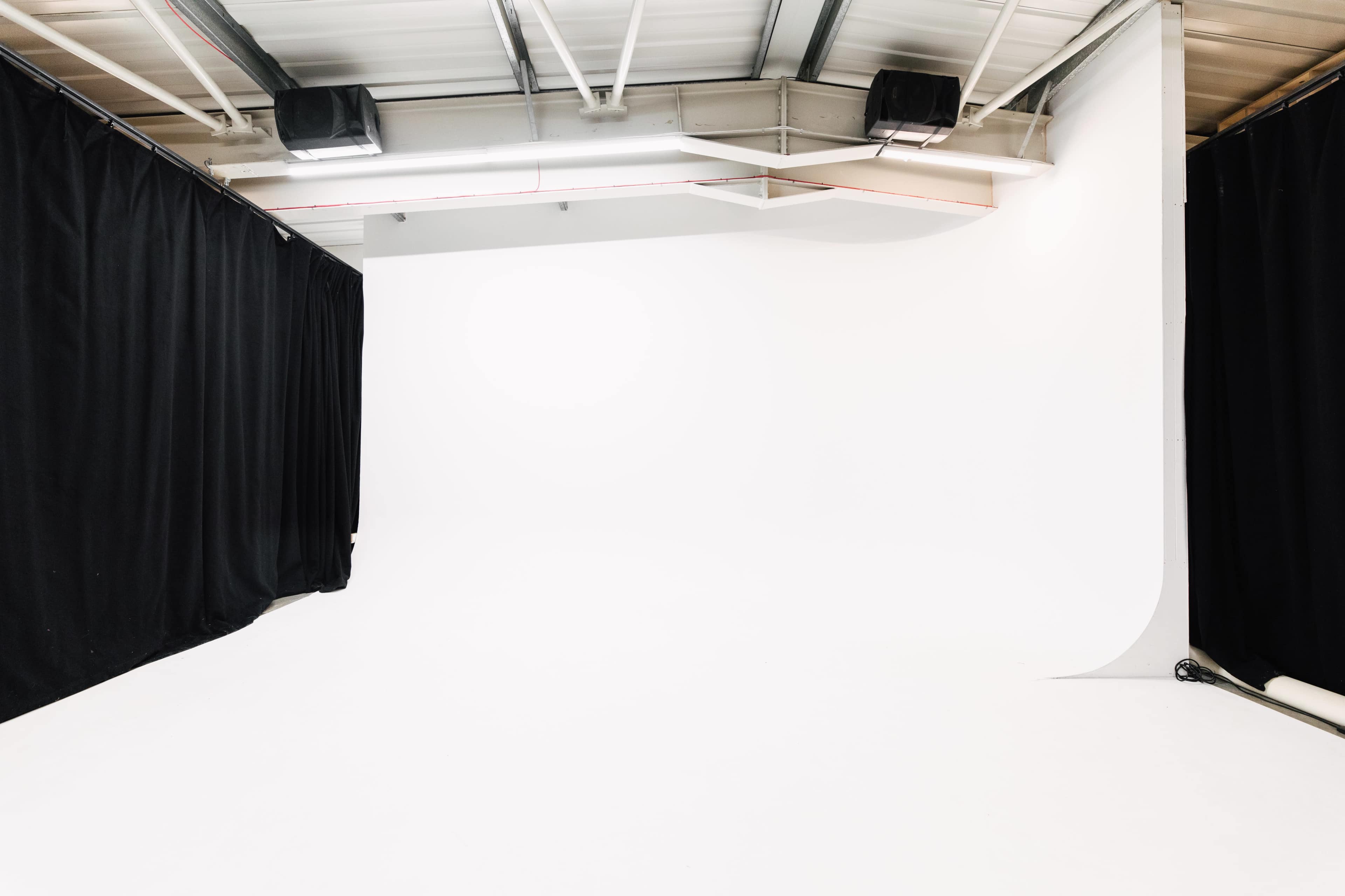 The image shows a blank photography studio with a white backdrop and black curtains on the sides.