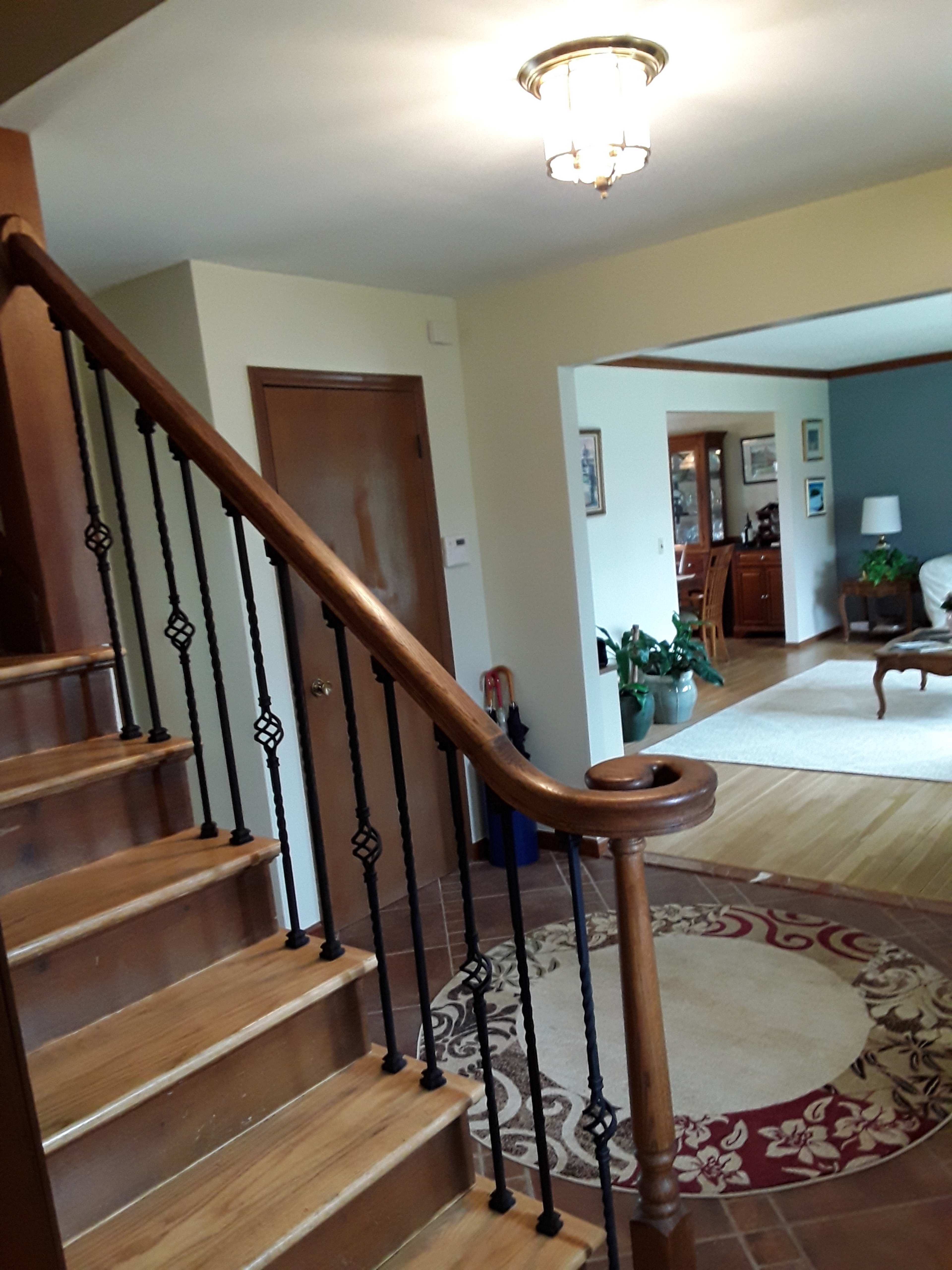 A staircase with a wooden railing leading to an upper level, adjacent to a living space with a rug and furnishings.