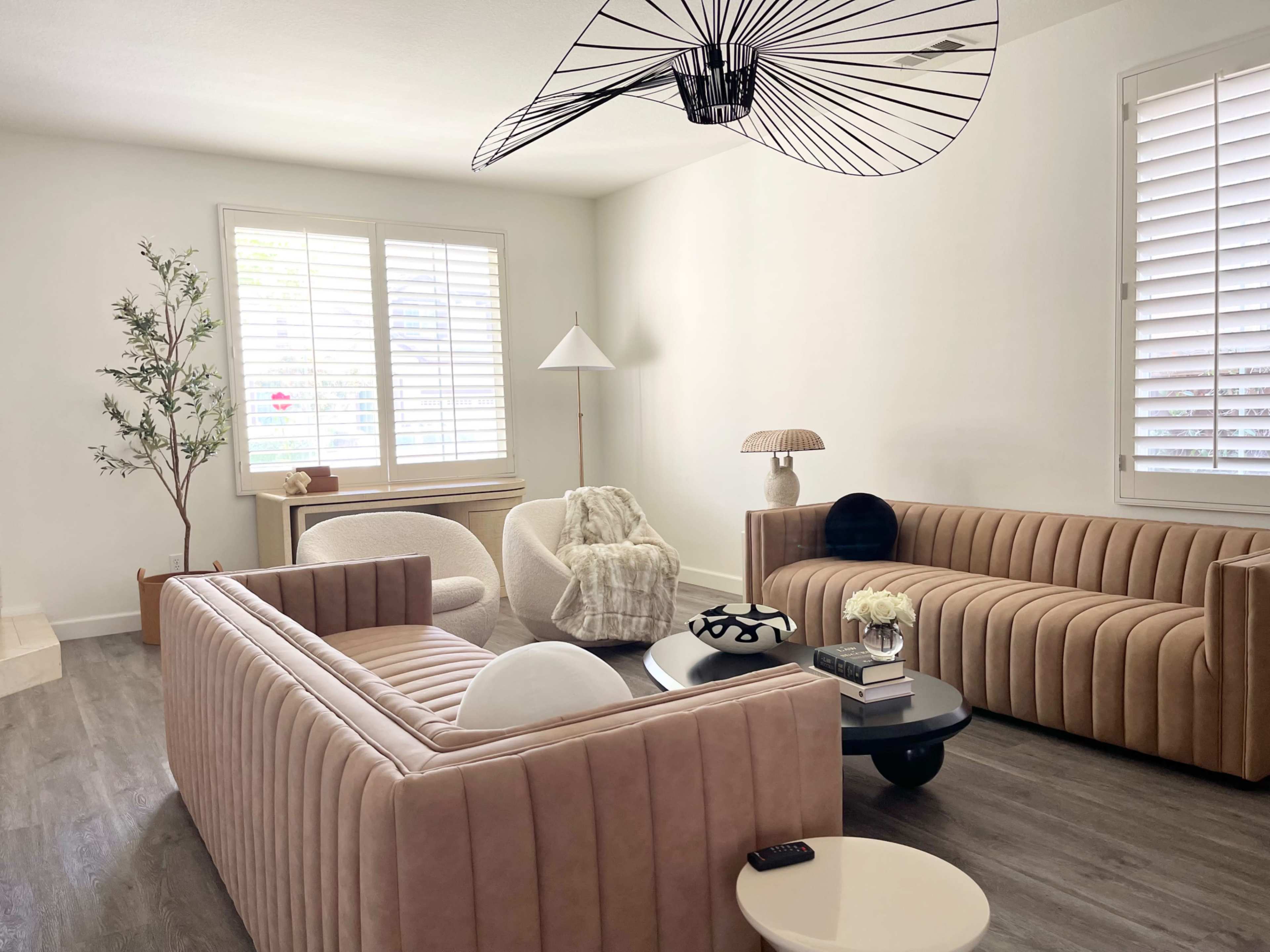 The room features two curved, upholstered sofas facing each other, a round coffee table in the center, and a mix of modern lighting and decorative elements.