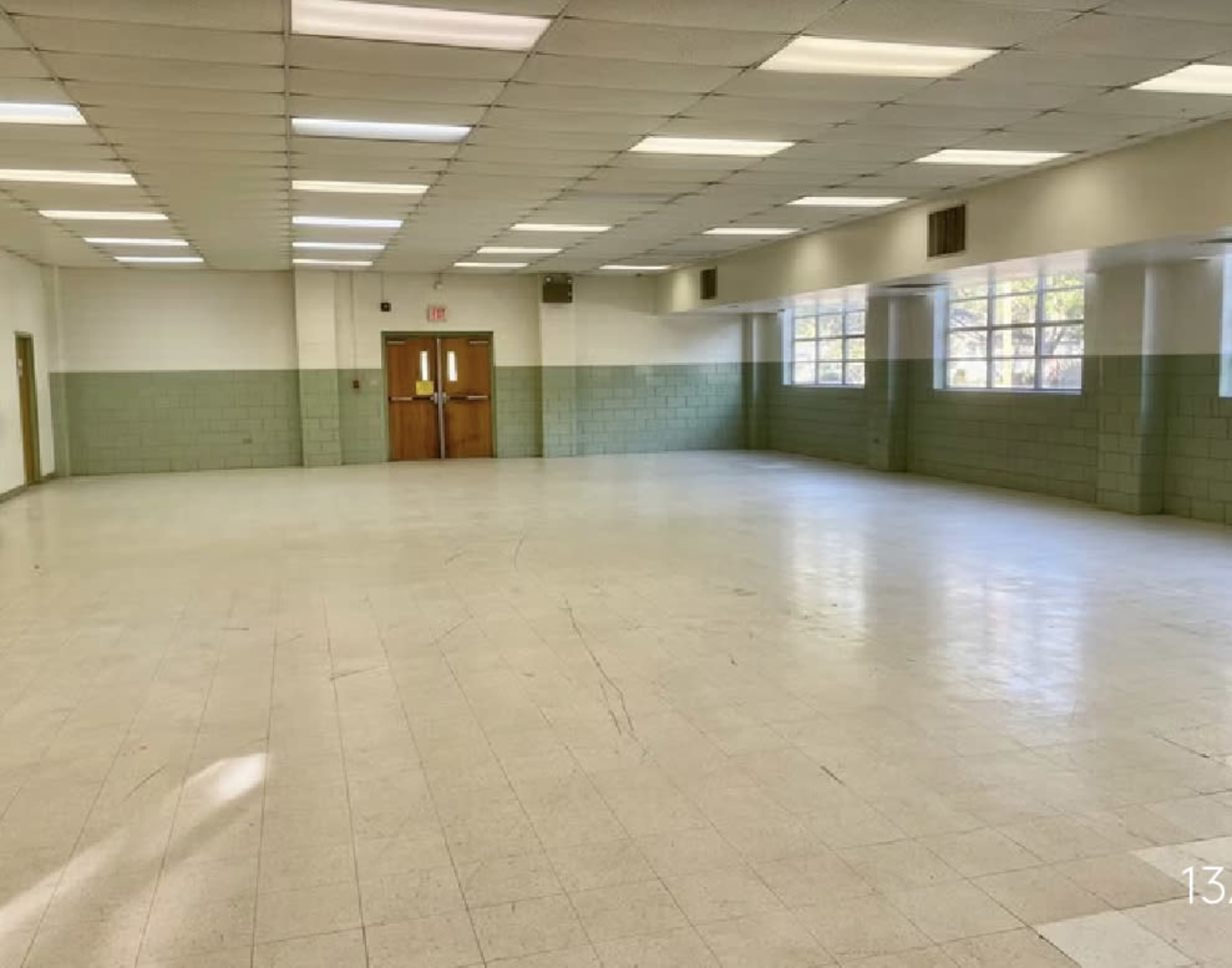 A vacant, well-lit room with tiled floors and large windows along one wall.