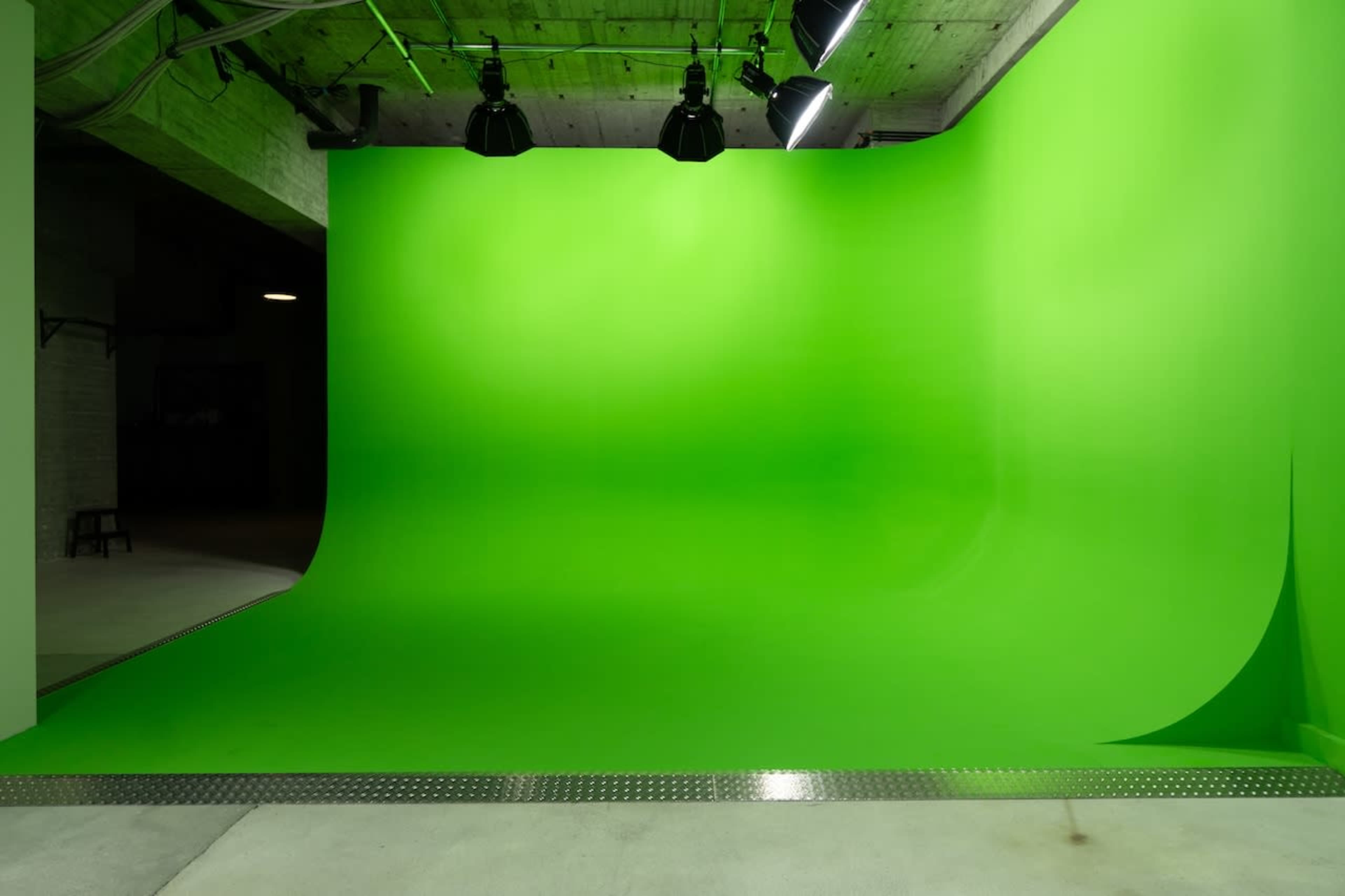 The image shows a spacious studio with a large green backdrop and overhead lighting.