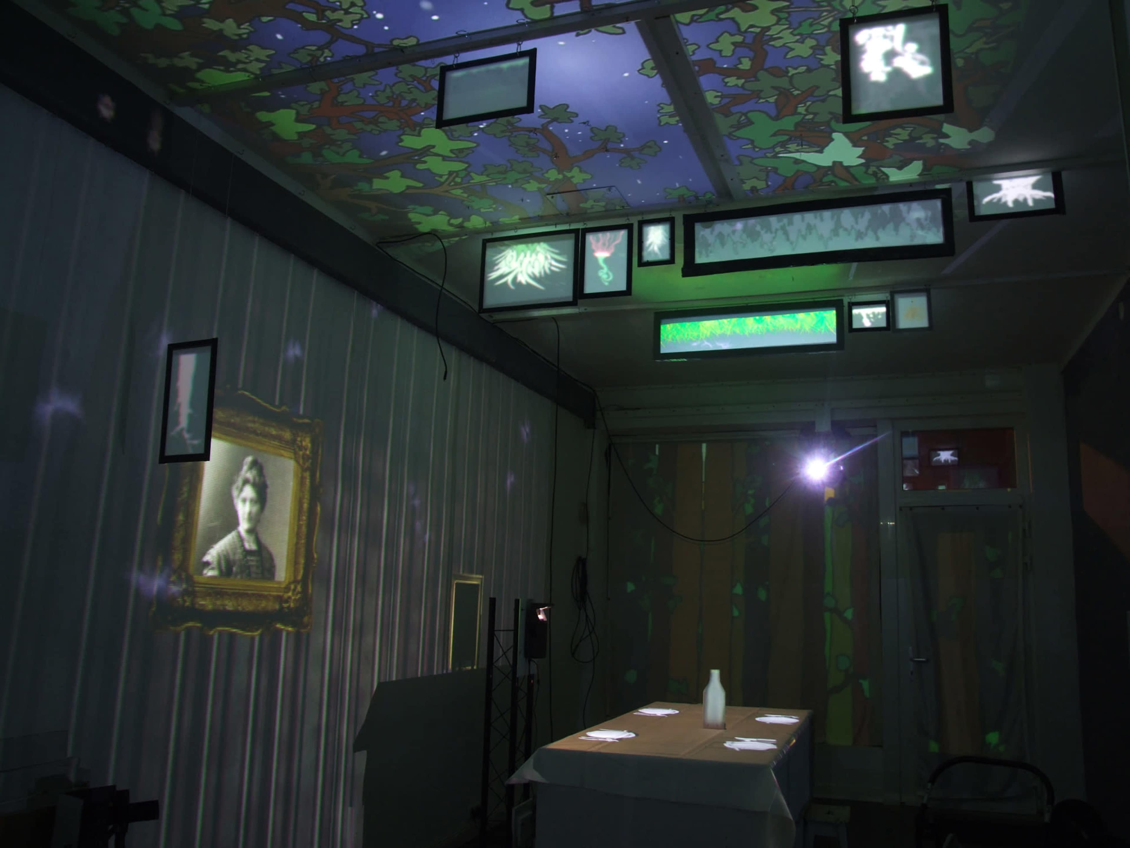 A dimly lit room with projected images on the walls and ceiling, featuring various frames and artwork alongside a table set for dining.
