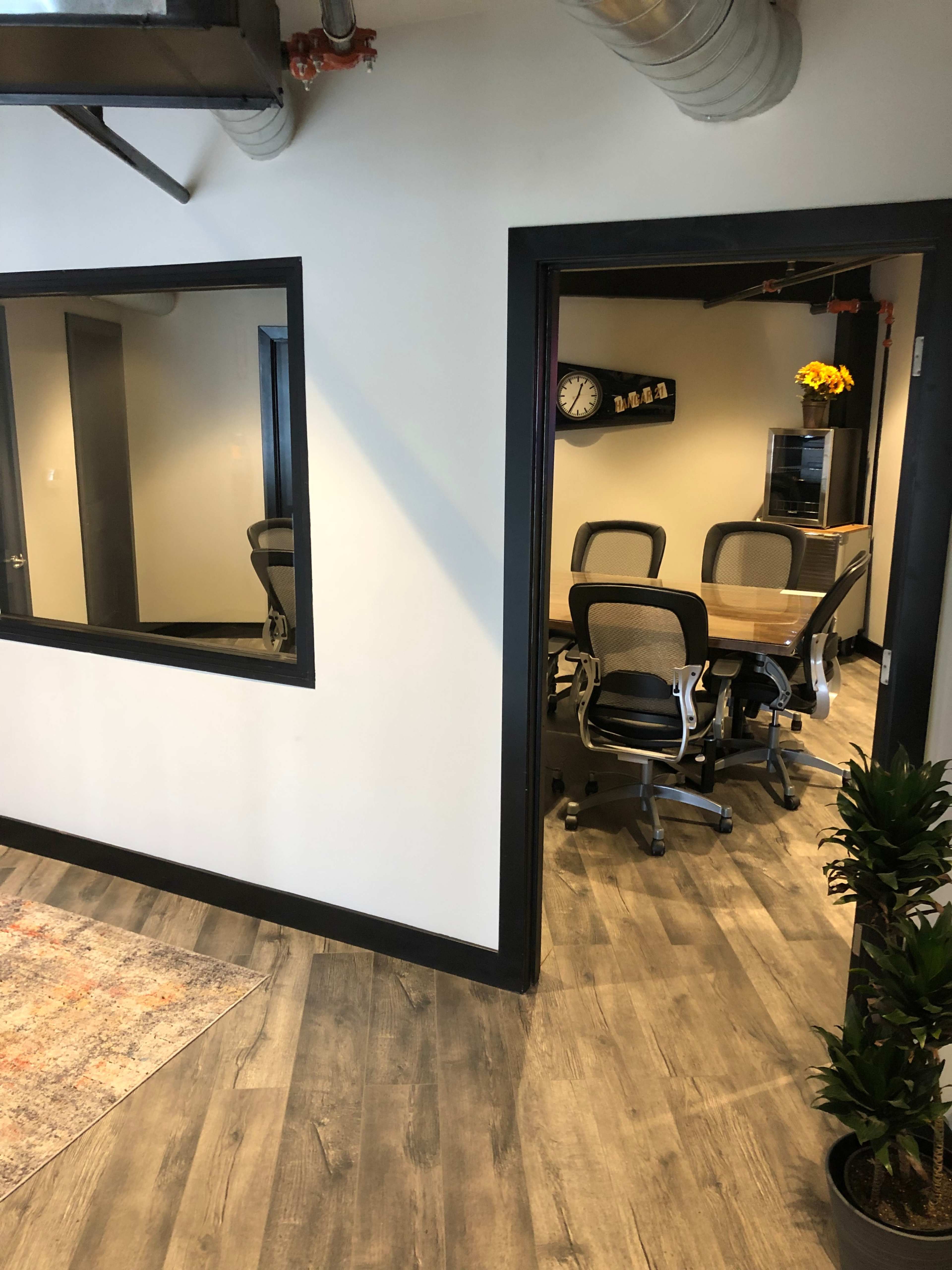 A modern office space with a meeting room visible through a glass window and a wooden floor leading to the room.