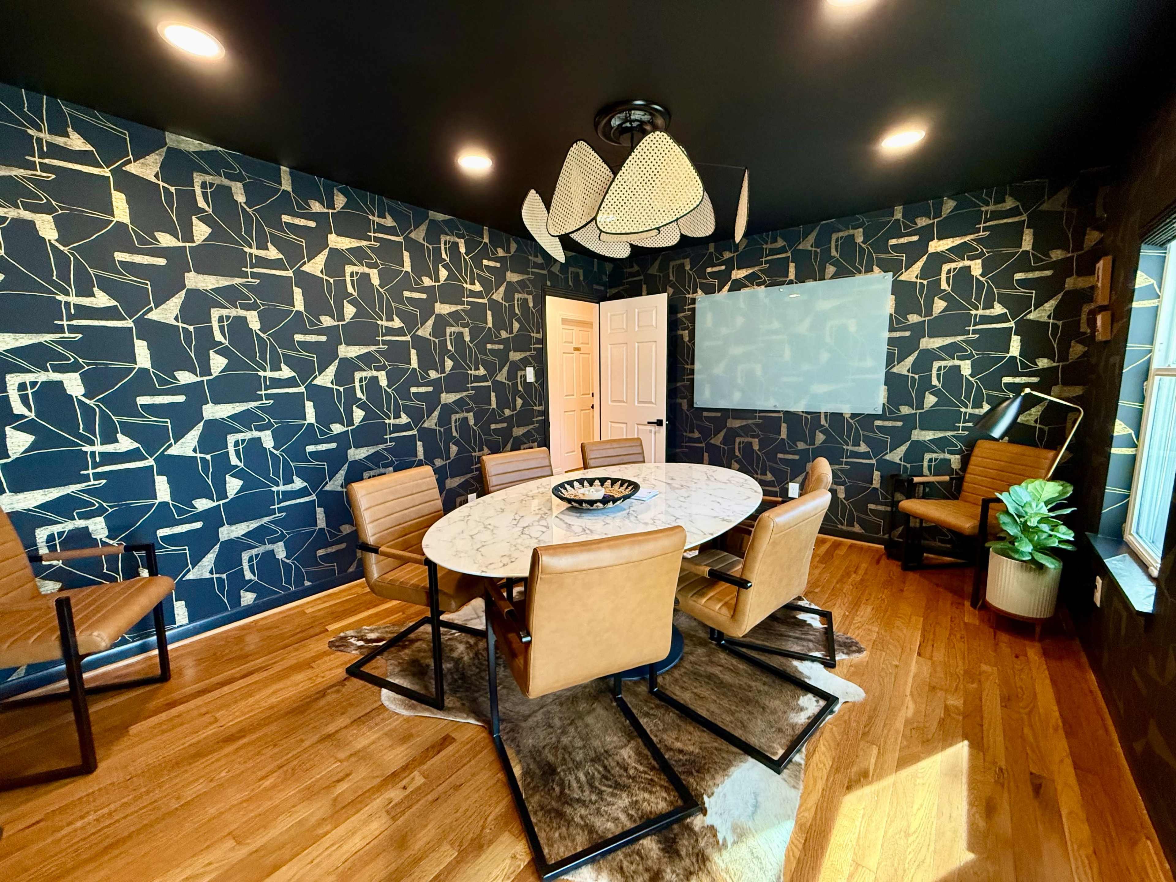 The image shows a modern dining room featuring a round marble table surrounded by six brown chairs, with a patterned black and gold accent wall and a large window.