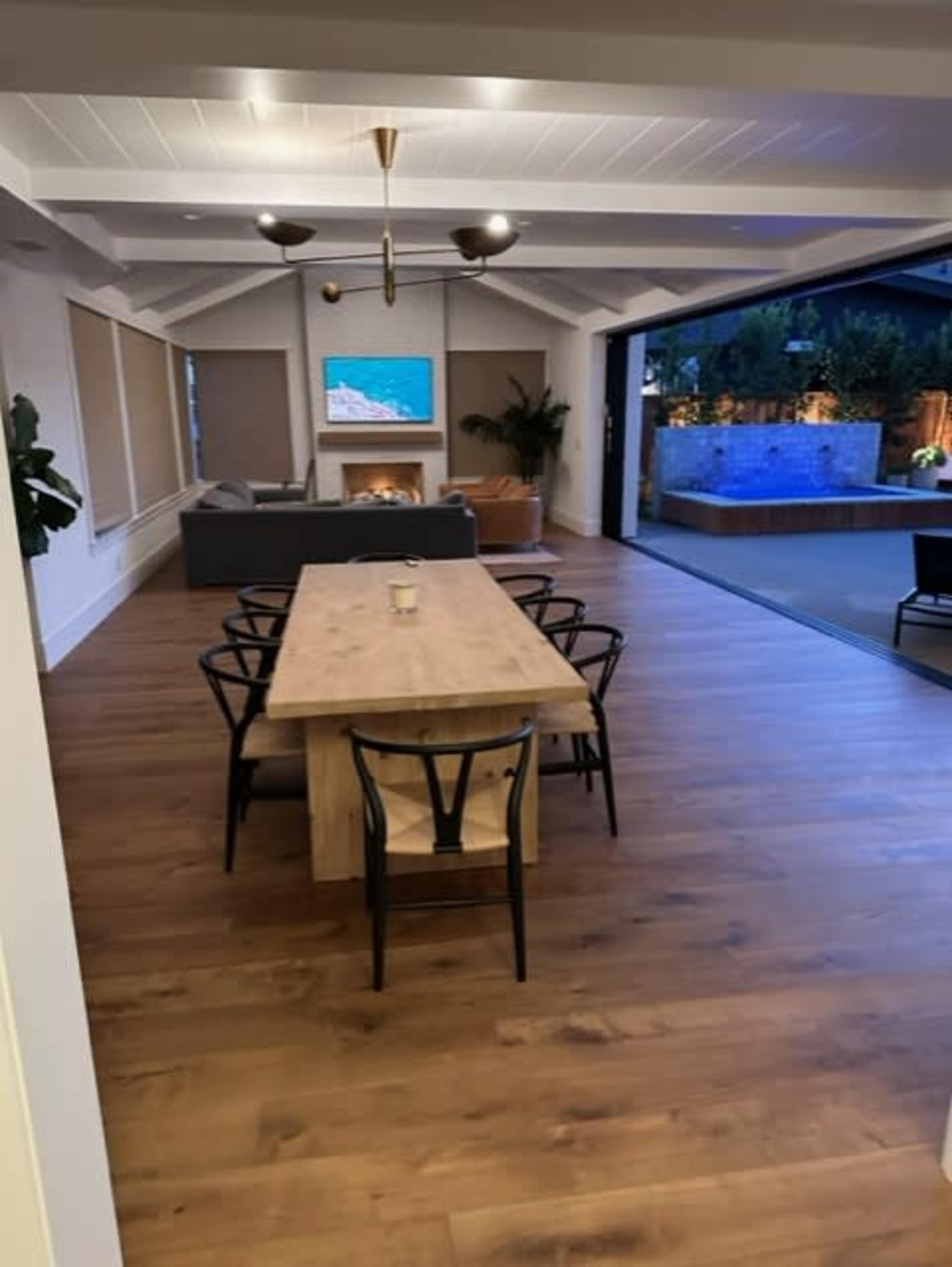 A modern open-concept living and dining area with a large wooden table, chairs, and a view of an outdoor space featuring a pool and a fireplace.