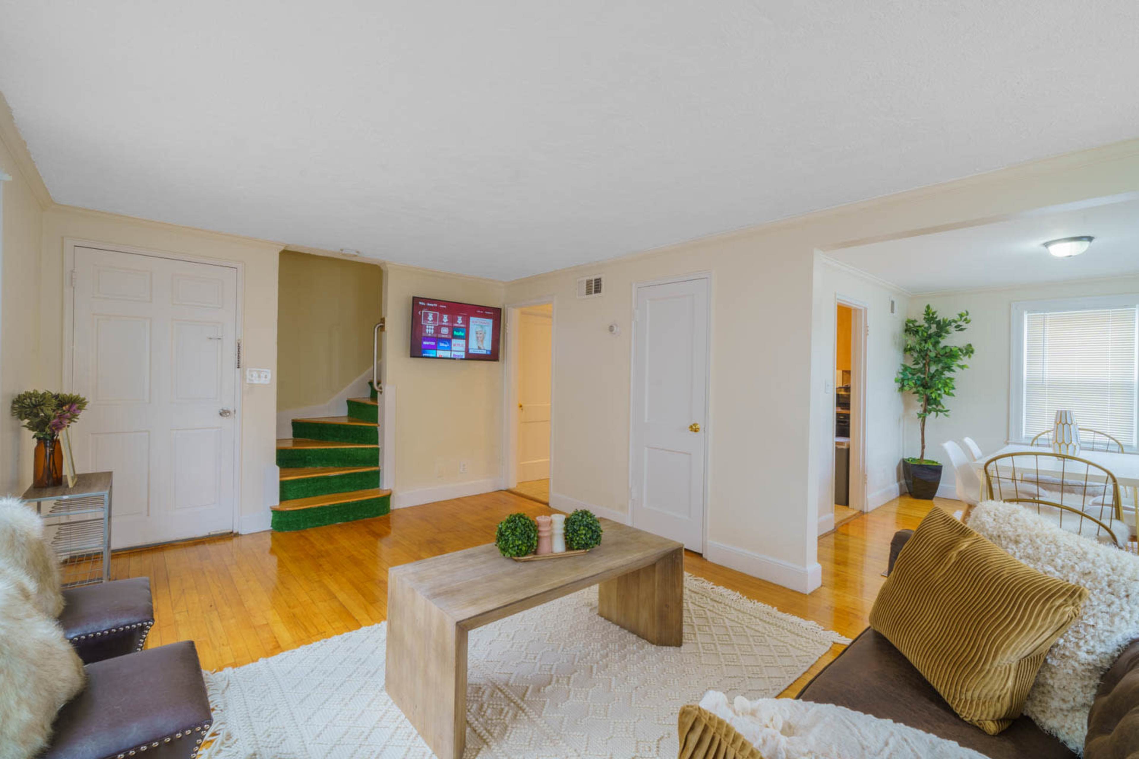 A living room with a coffee table, seating area, and a staircase leading to an upper level, alongside a wall-mounted television.