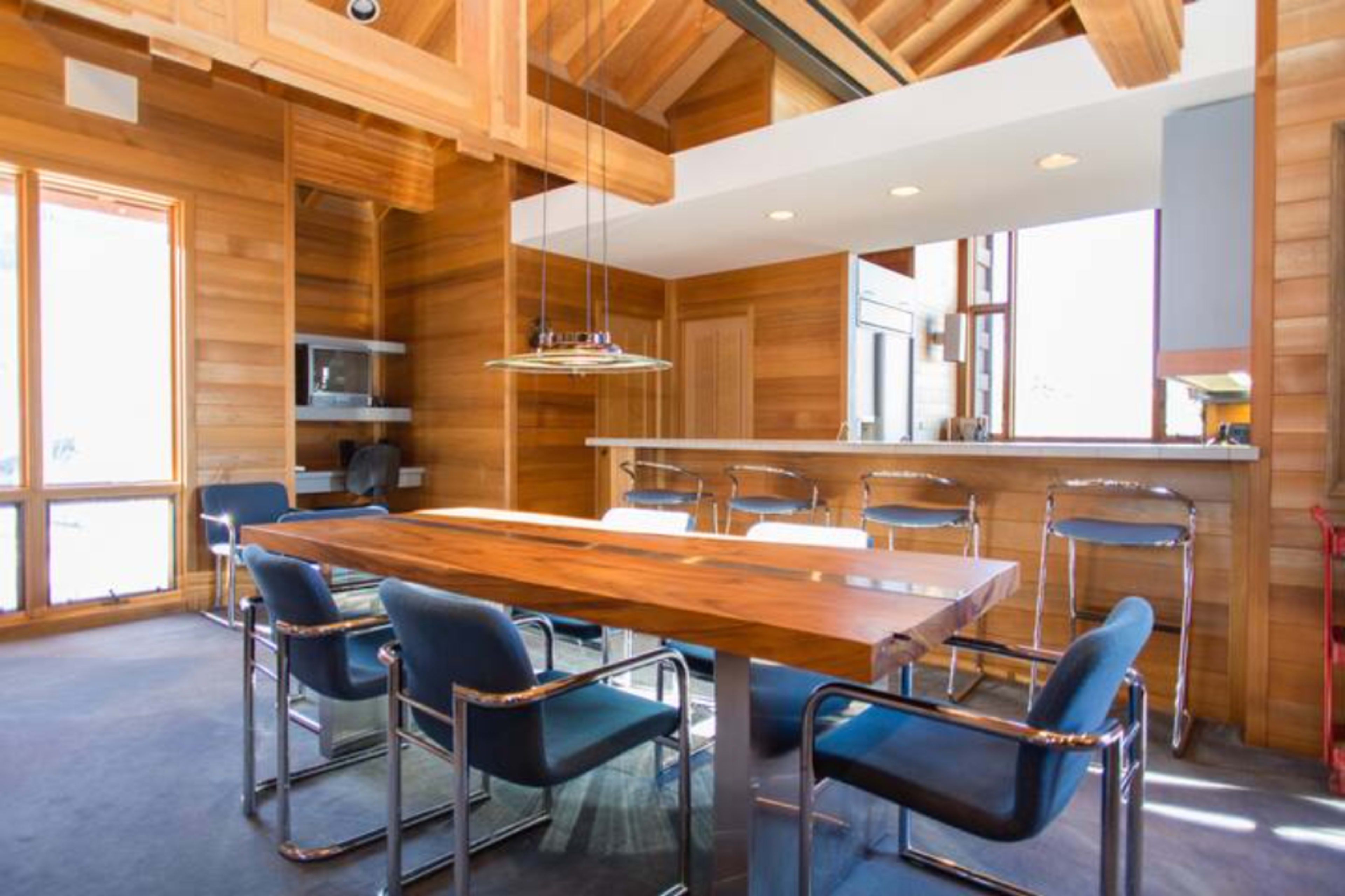 A modern dining area with a wooden table surrounded by metal-framed chairs, set in a space with wood-paneled walls and large windows.