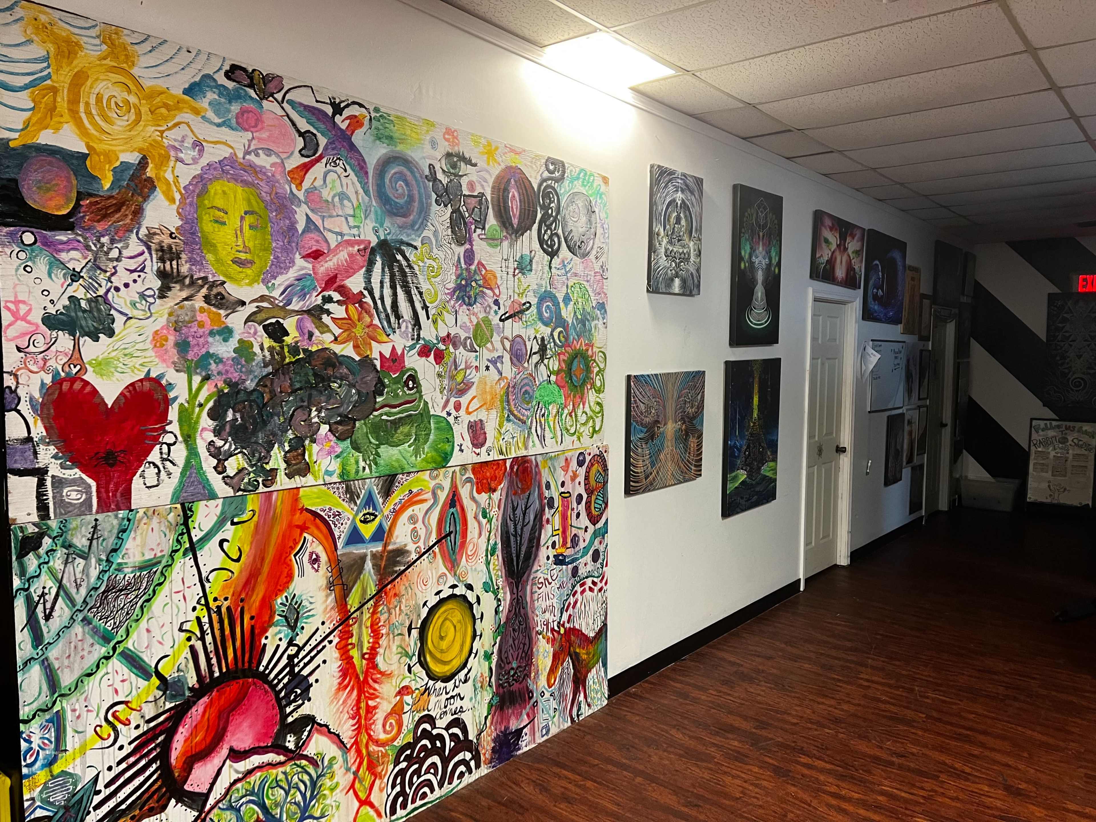 The image shows a hallway featuring colorful murals and various artworks displayed on the walls.