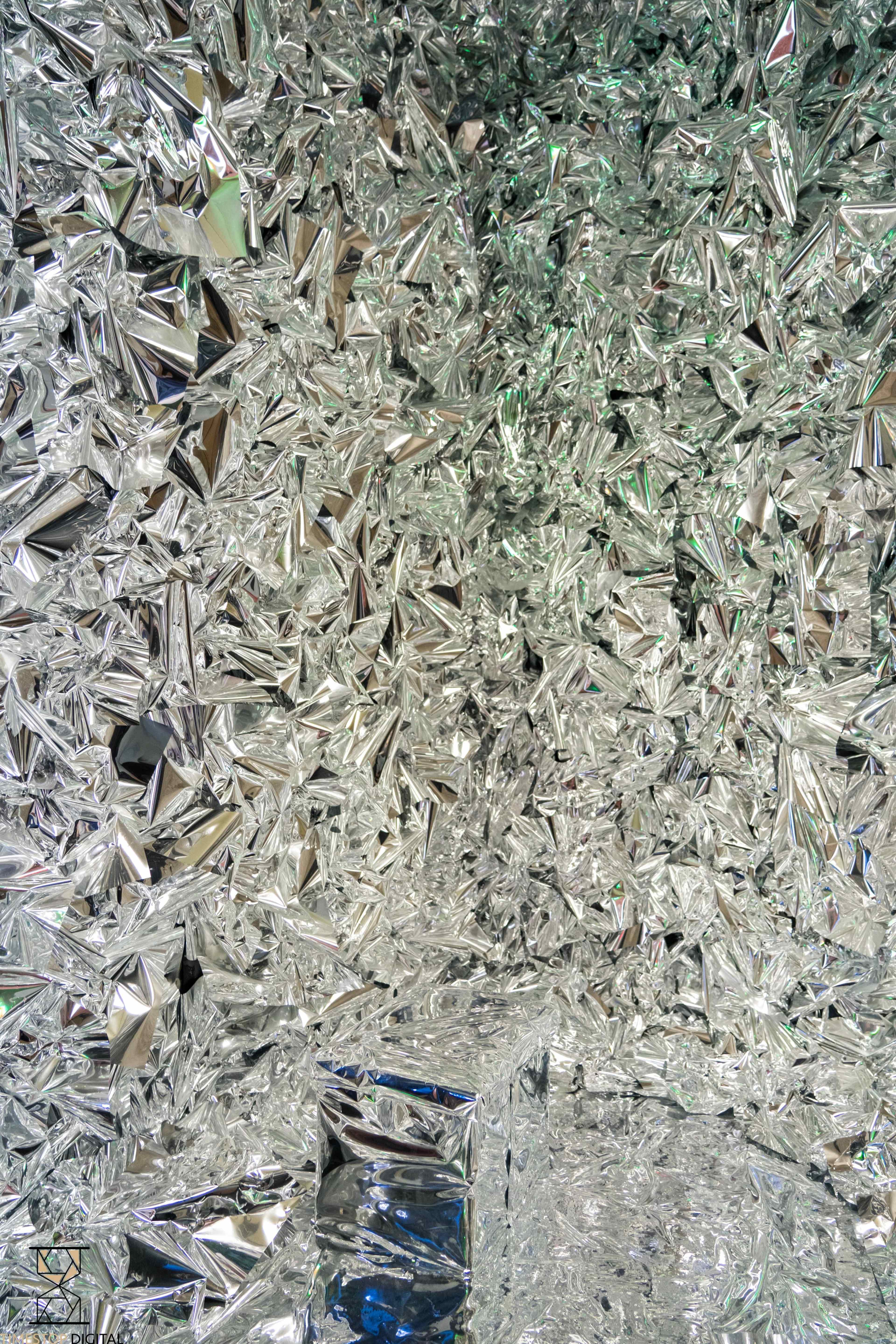 The image shows a surface covered in a multitude of reflective, angular, silver-colored geometric shapes.