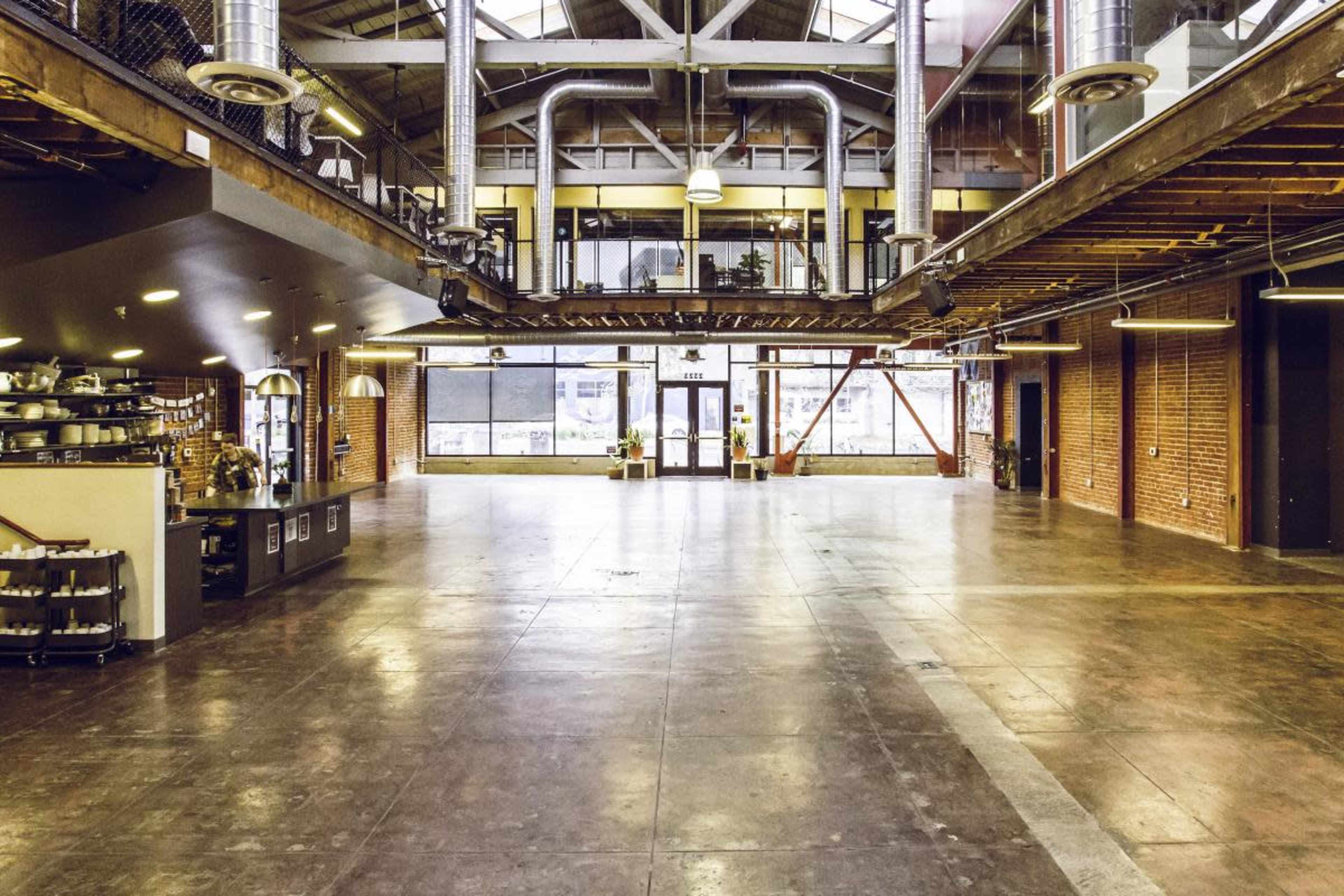 A spacious industrial-style interior with polished concrete floors, large windows, exposed metal beams, and a bar area on the left.