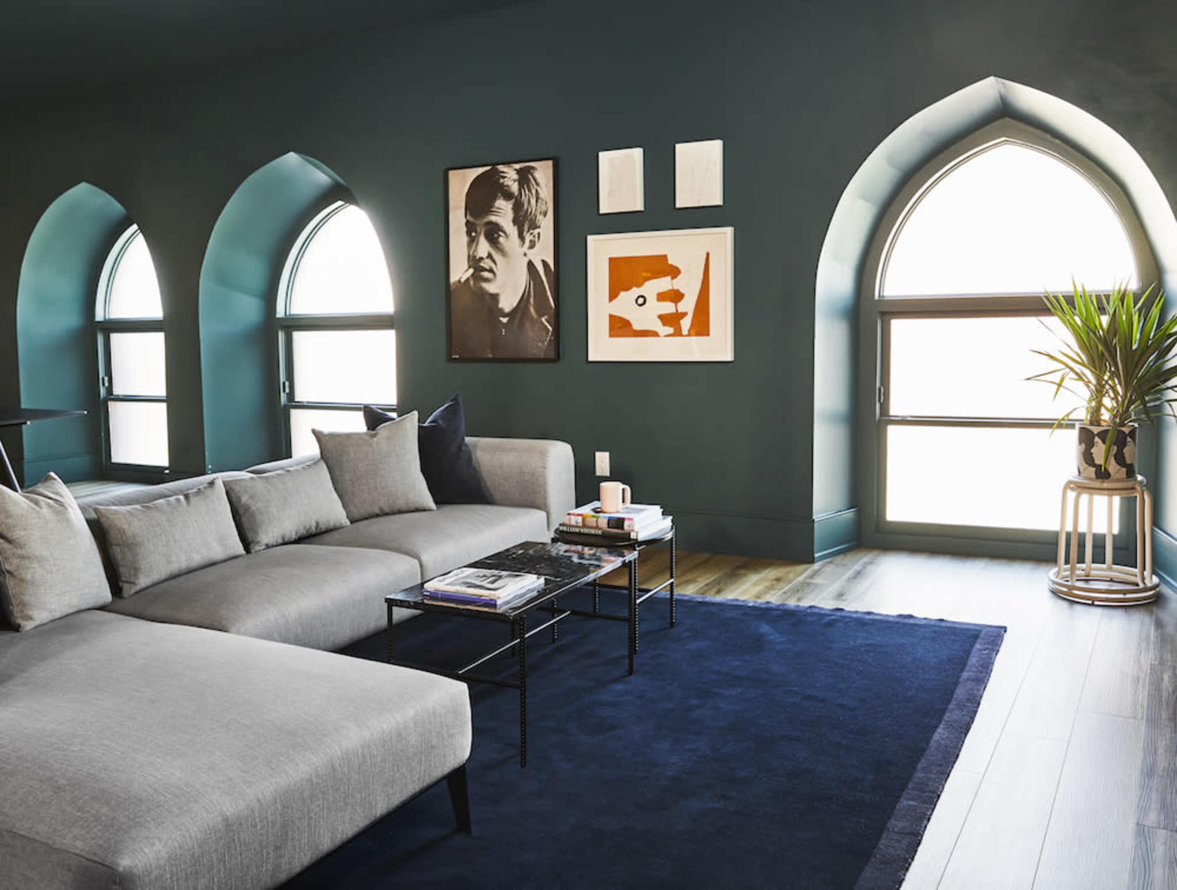 The image shows a modern living room featuring a grey sectional couch, a black coffee table with books, and large arched windows that allow natural light to enter.