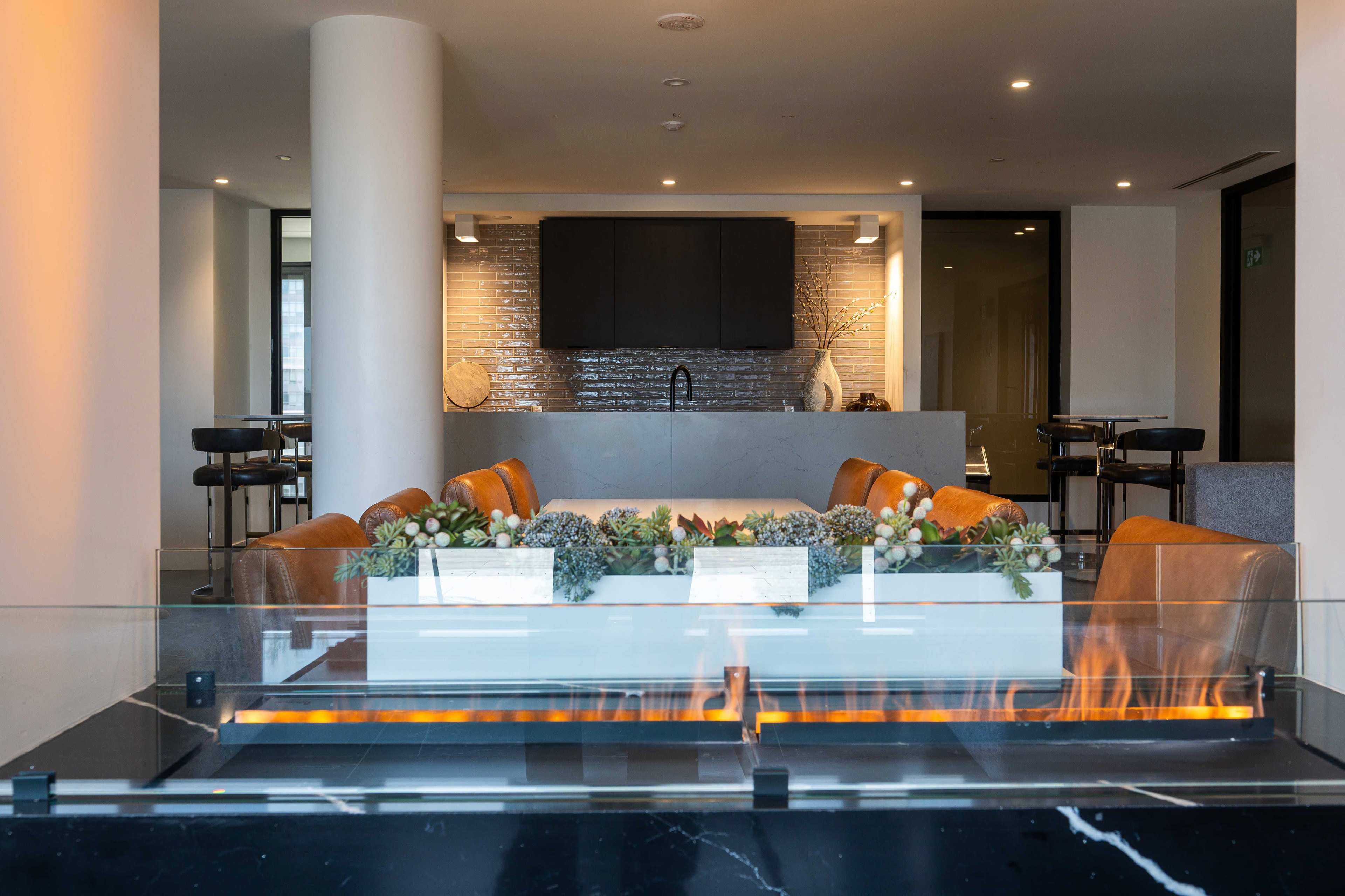 The image shows a modern interior space featuring a kitchen area with a stone countertop, a central planter with plants, and seating arrangements in the background.
