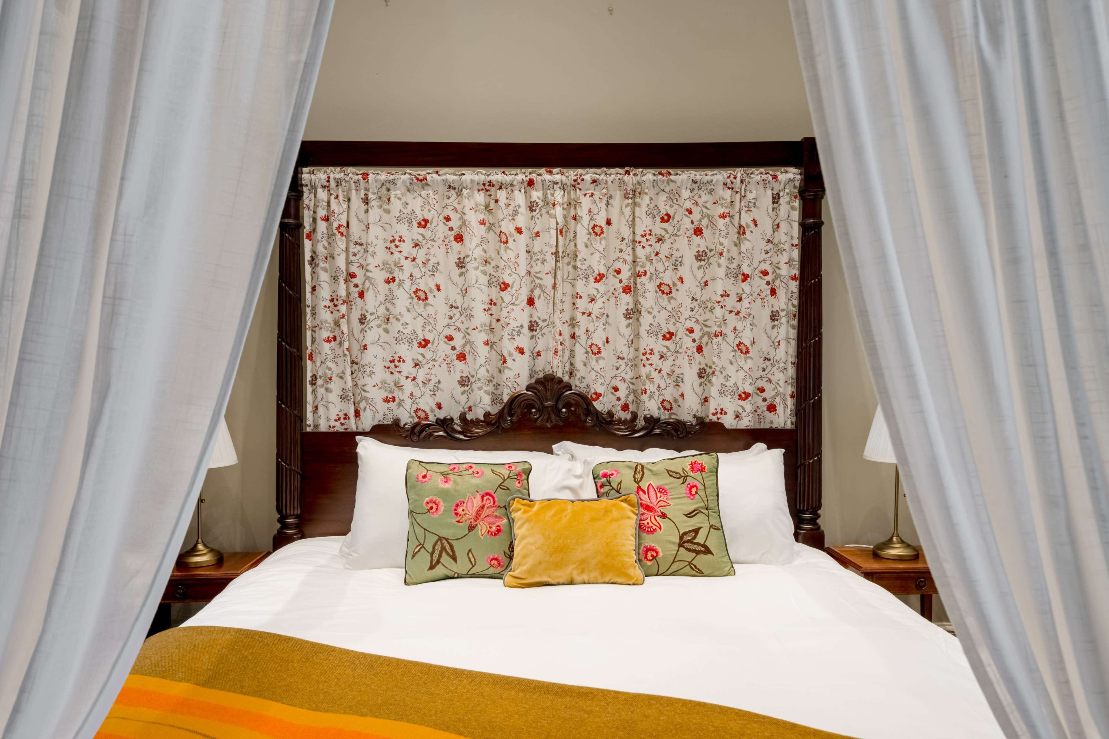 The image shows a cozy bedroom with a wooden bed frame, decorative pillows, and floral curtains.