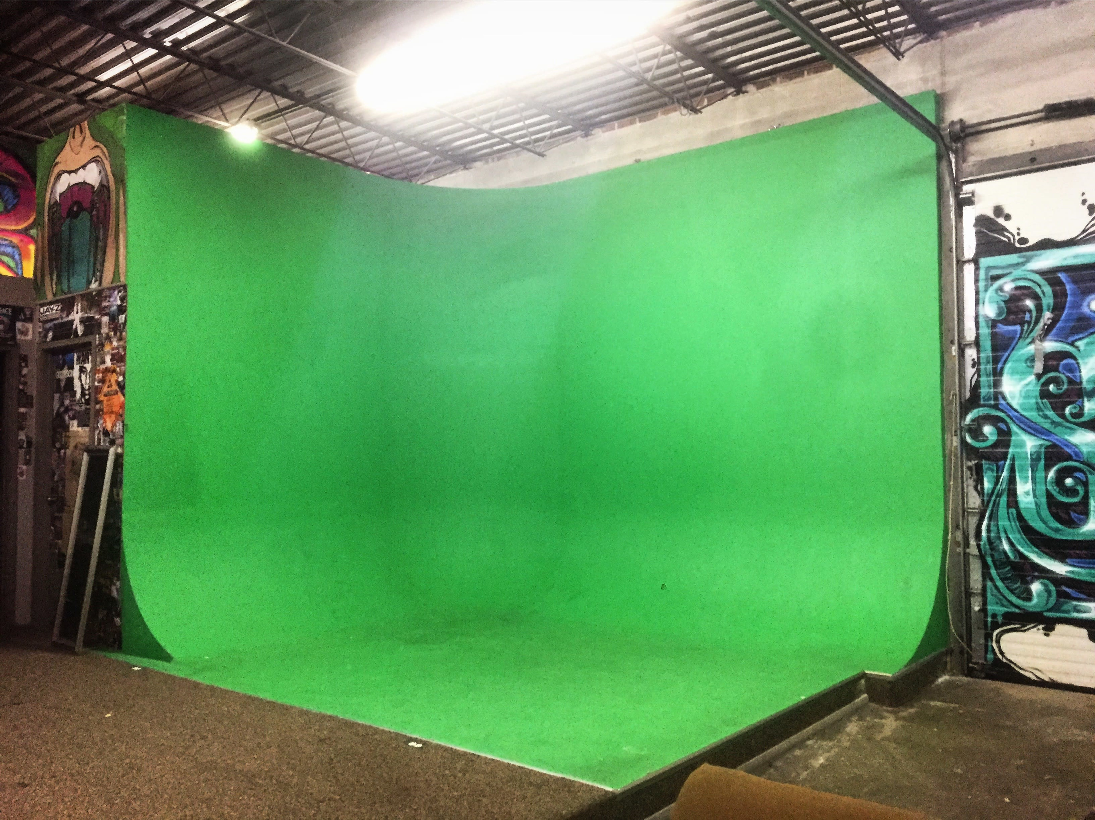 The image shows a green screen setup in an indoor studio with colorful graffiti on the walls.