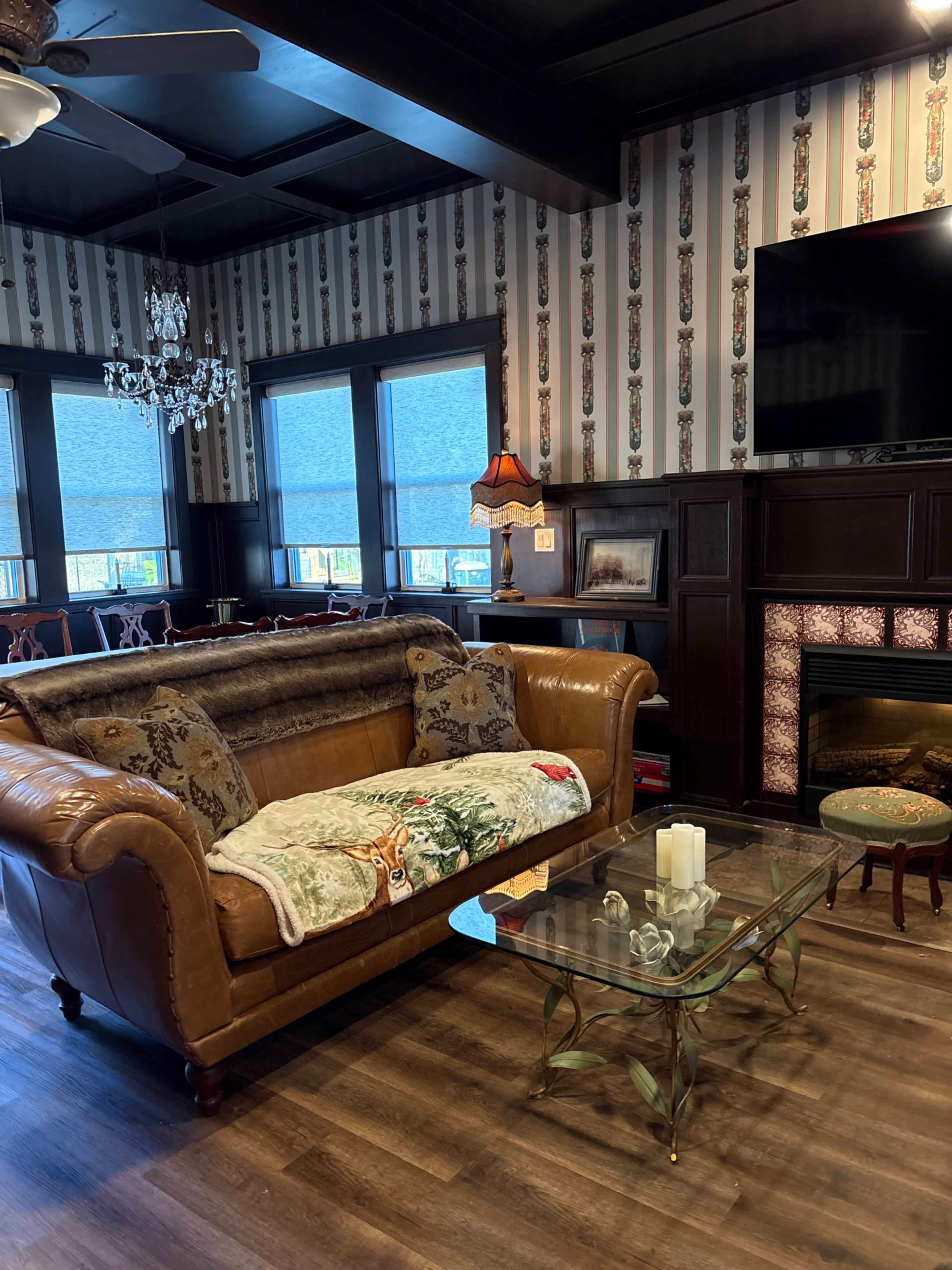The image shows a cozy living area featuring a leather sofa adorned with a decorative throw, a glass coffee table, and a fireplace, all set against a wallpapered wall.