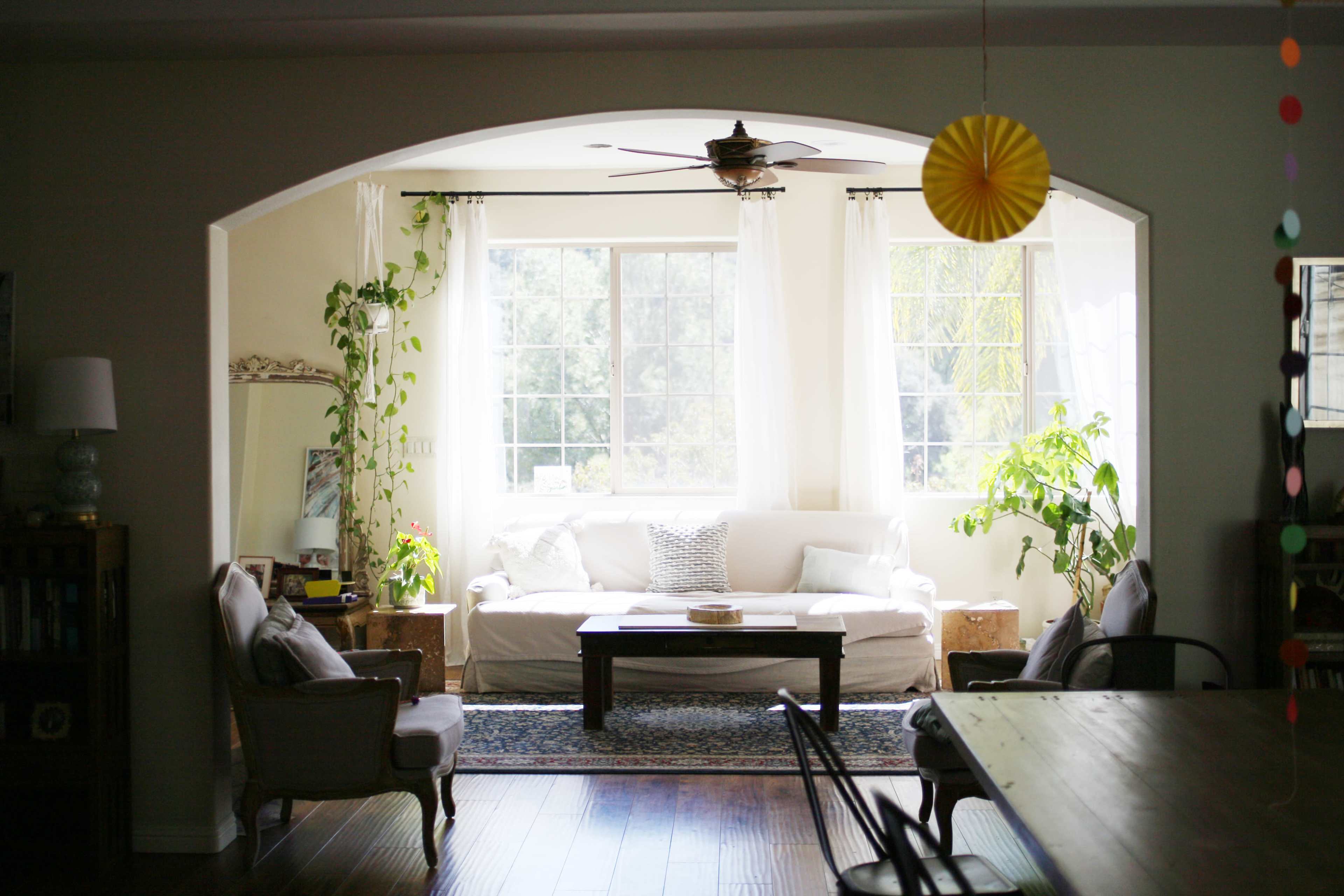 A bright living room with a white sofa, a coffee table, and large windows framed by light curtains.