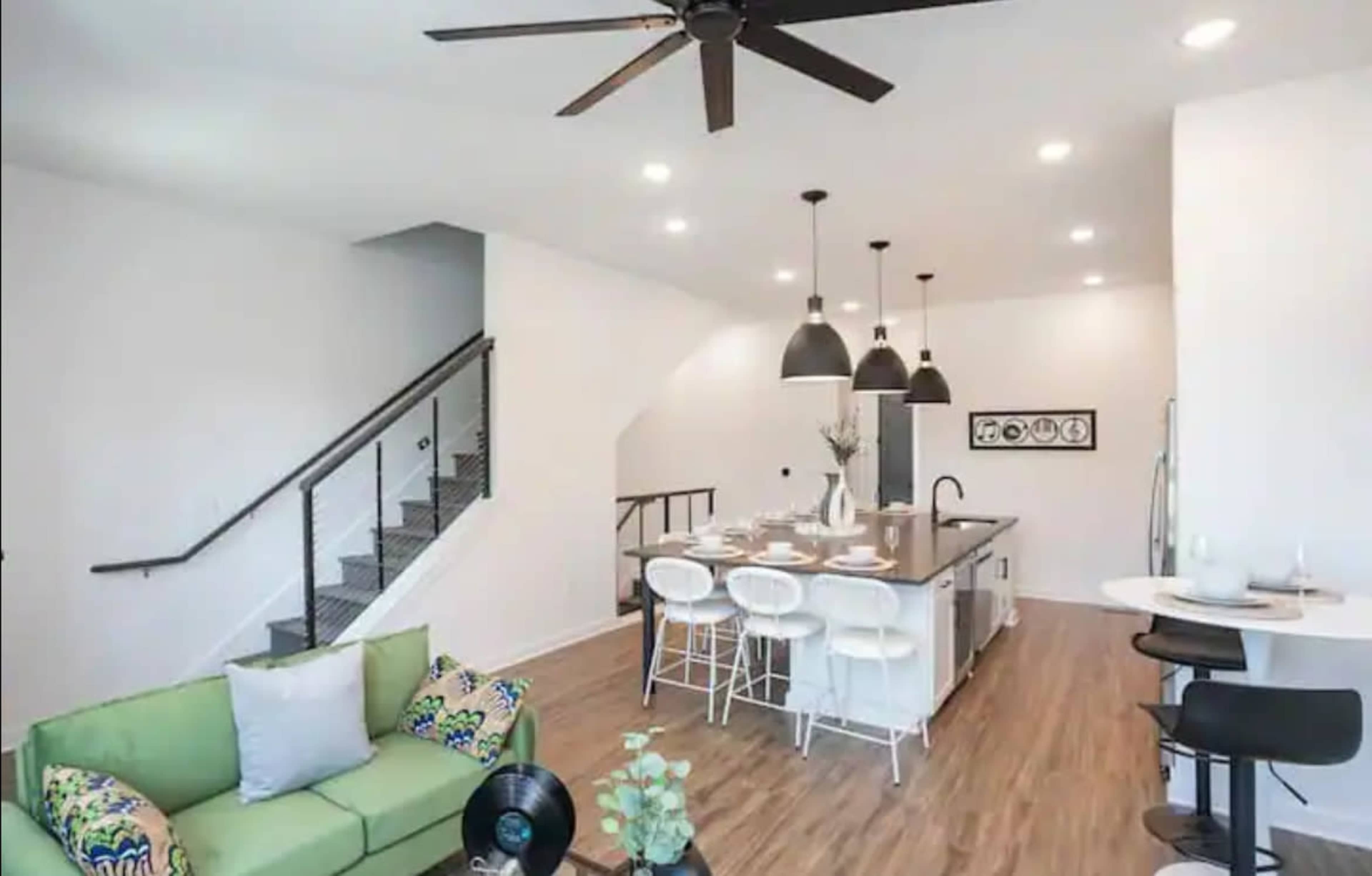 A modern open-concept kitchen and living area with a green couch, dining table, and a staircase in the background.