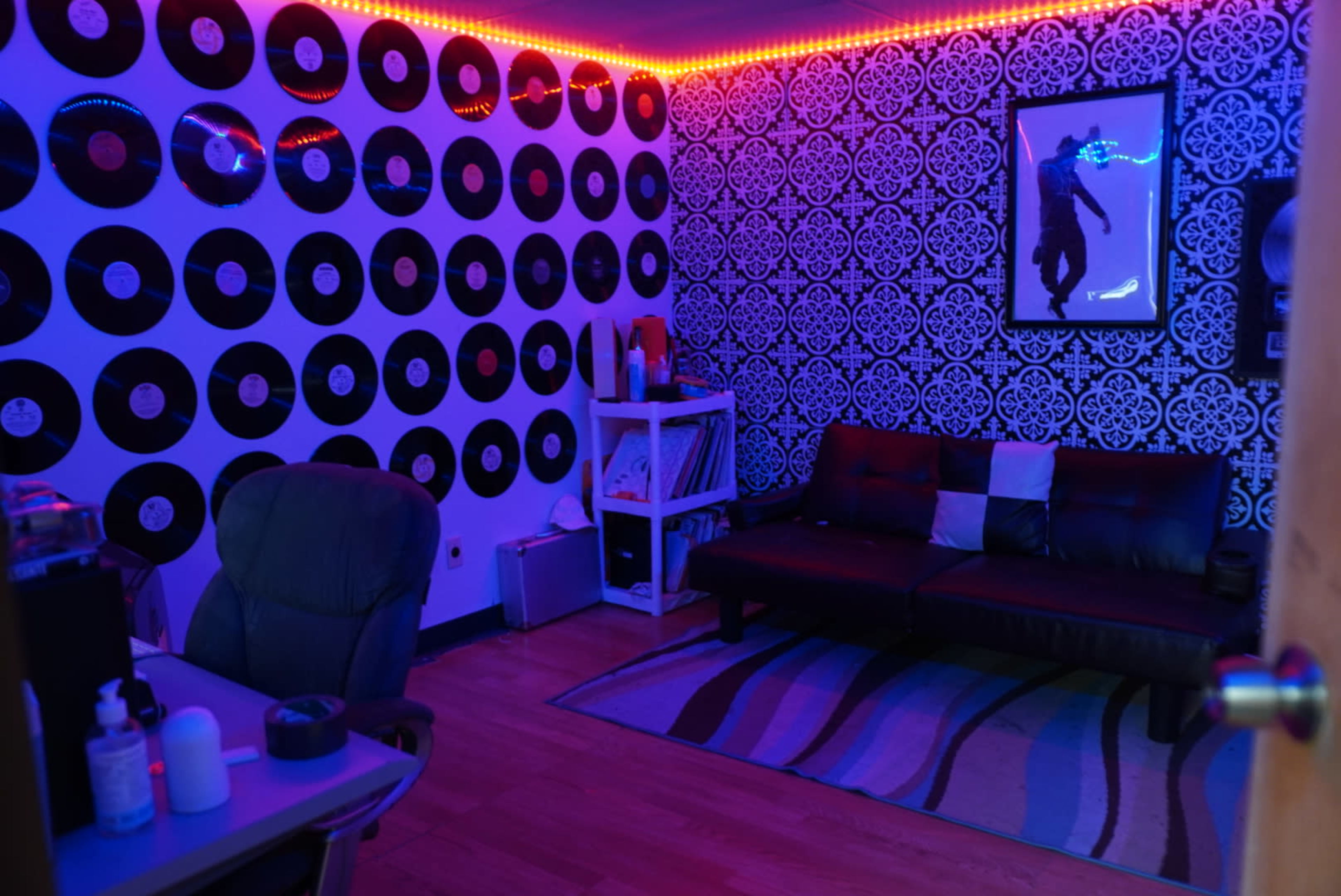 The room features a wall covered in vinyl records, a dark sofa, a rug, and blue LED lighting.