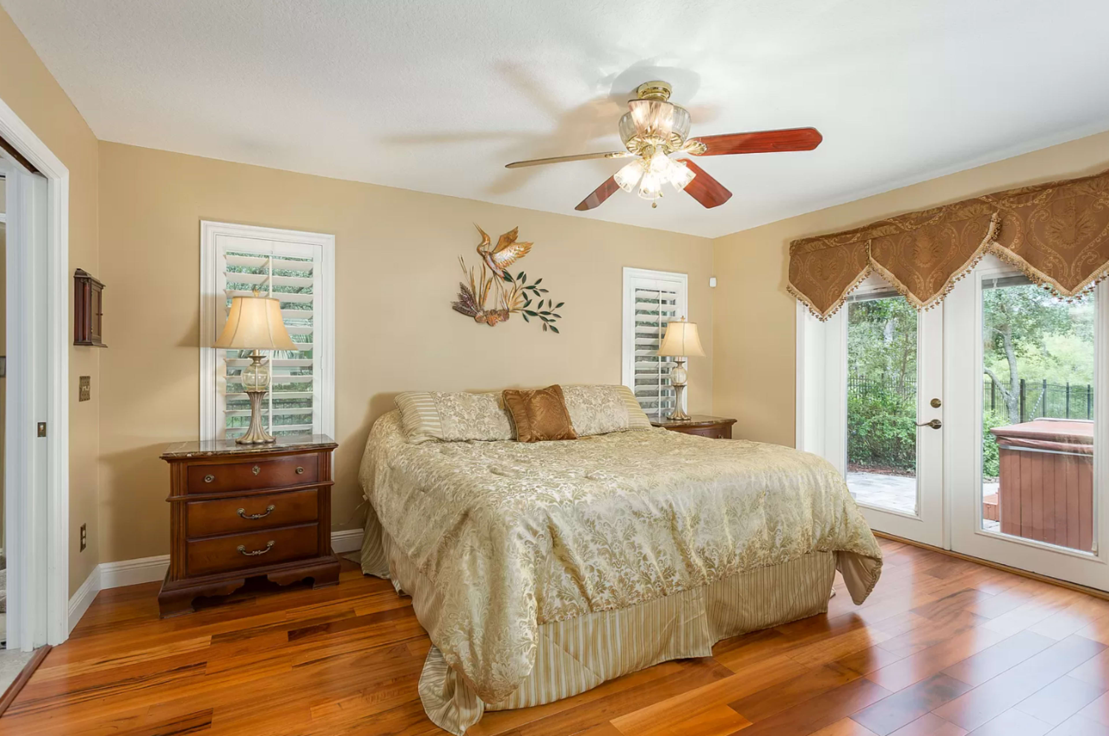 The bedroom features a large bed with a decorative cover, two lamps on wooden nightstands, and sliding glass doors leading to an outdoor area.