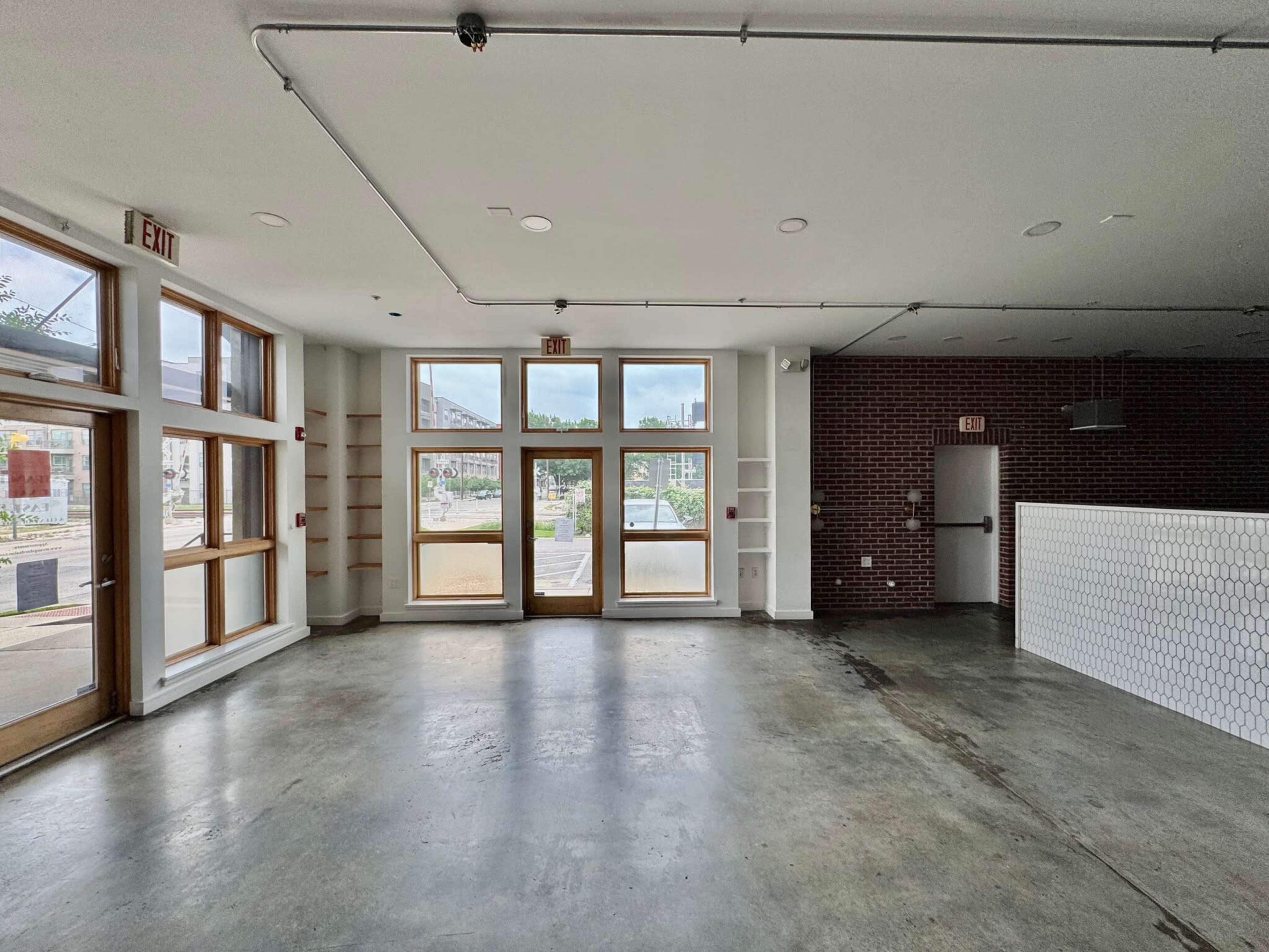 The image shows an empty commercial space with large front windows and concrete flooring.