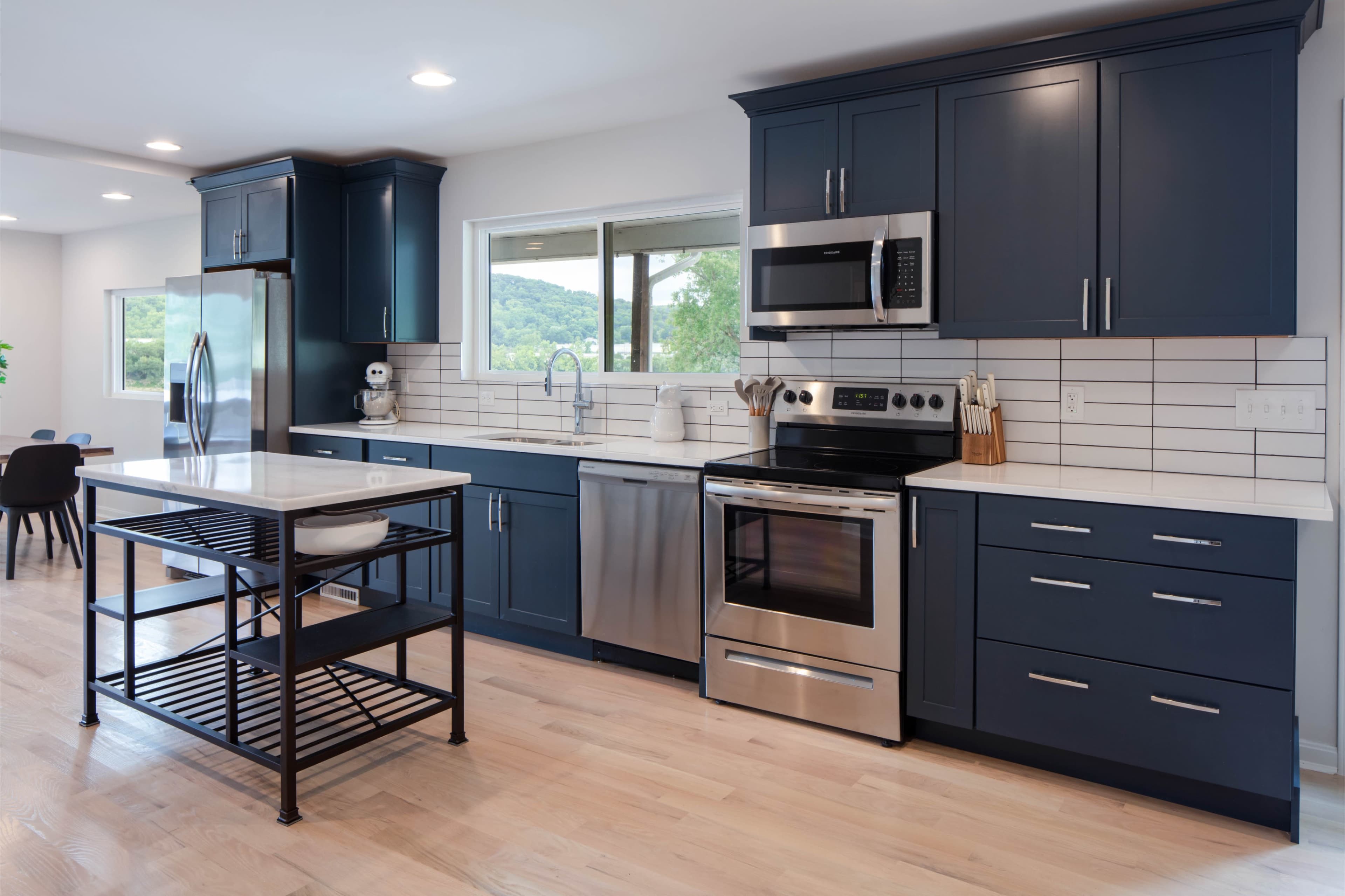 A modern kitchen with navy blue cabinets, stainless steel appliances, and an island with a black metal frame.