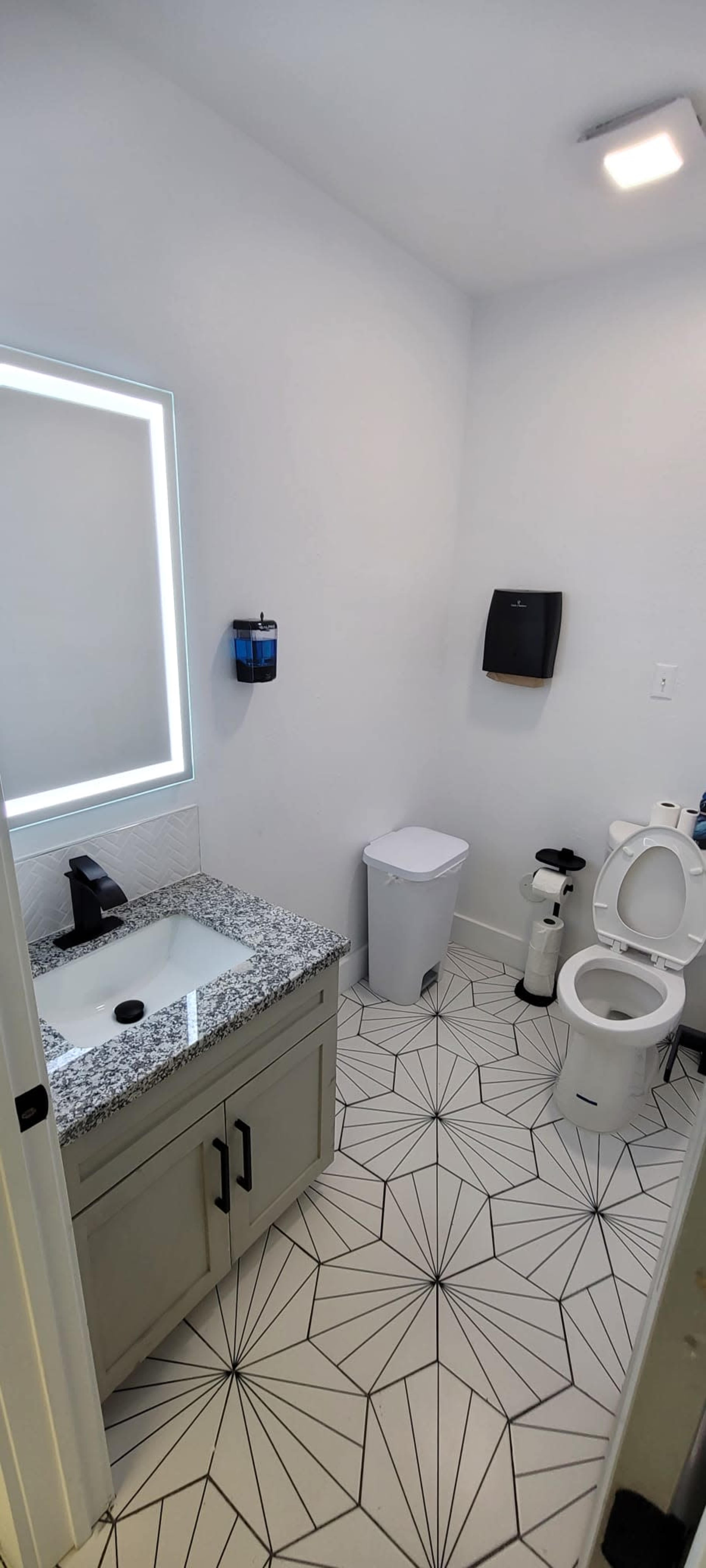A modern bathroom featuring a granite countertop sink, a toilet, and geometric tile flooring.