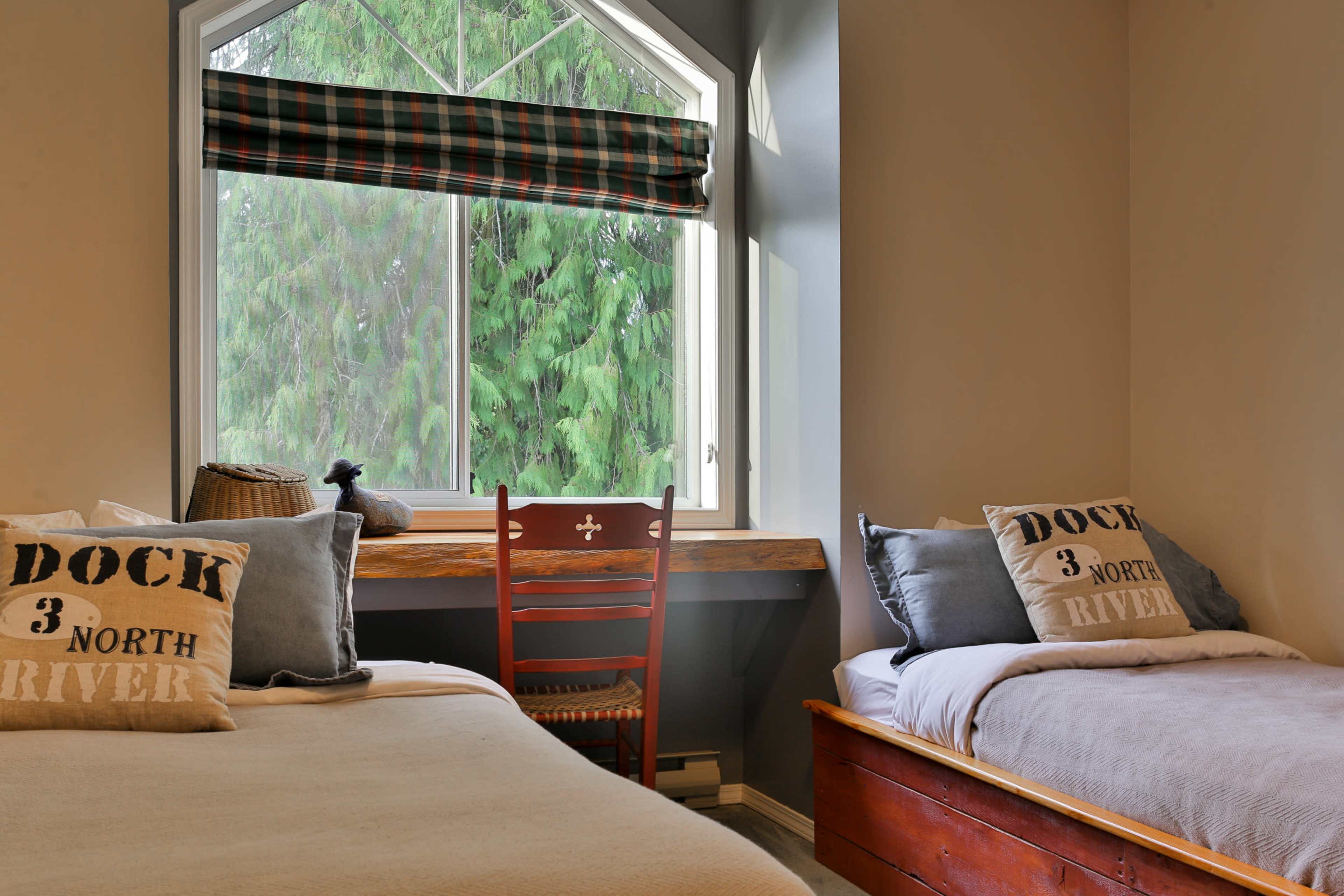 A cozy bedroom with two beds, a wooden chair, and a window overlooking greenery.