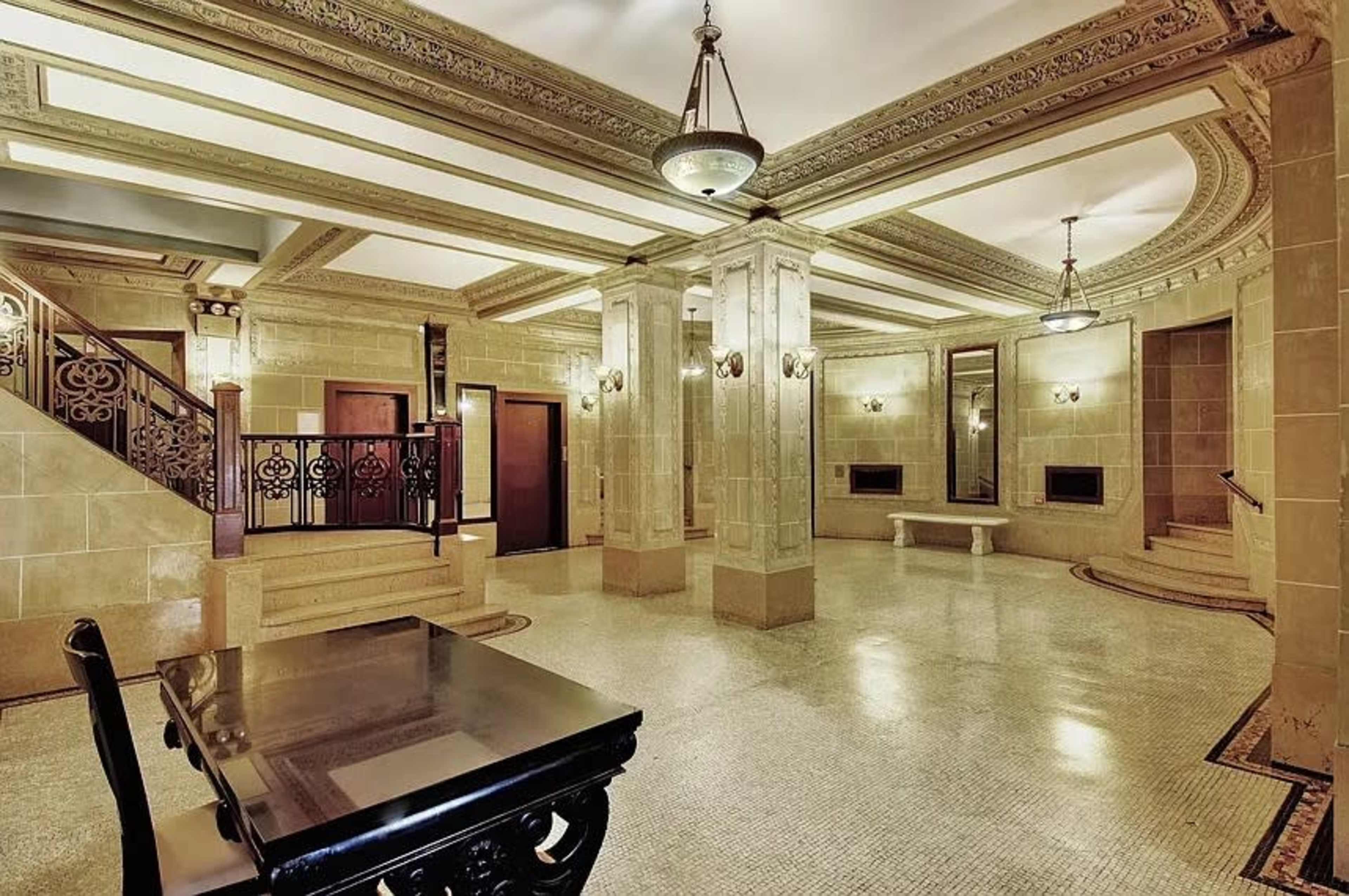 The image shows a spacious lobby with intricately designed ceilings, marble columns, and a patterned tiled floor.