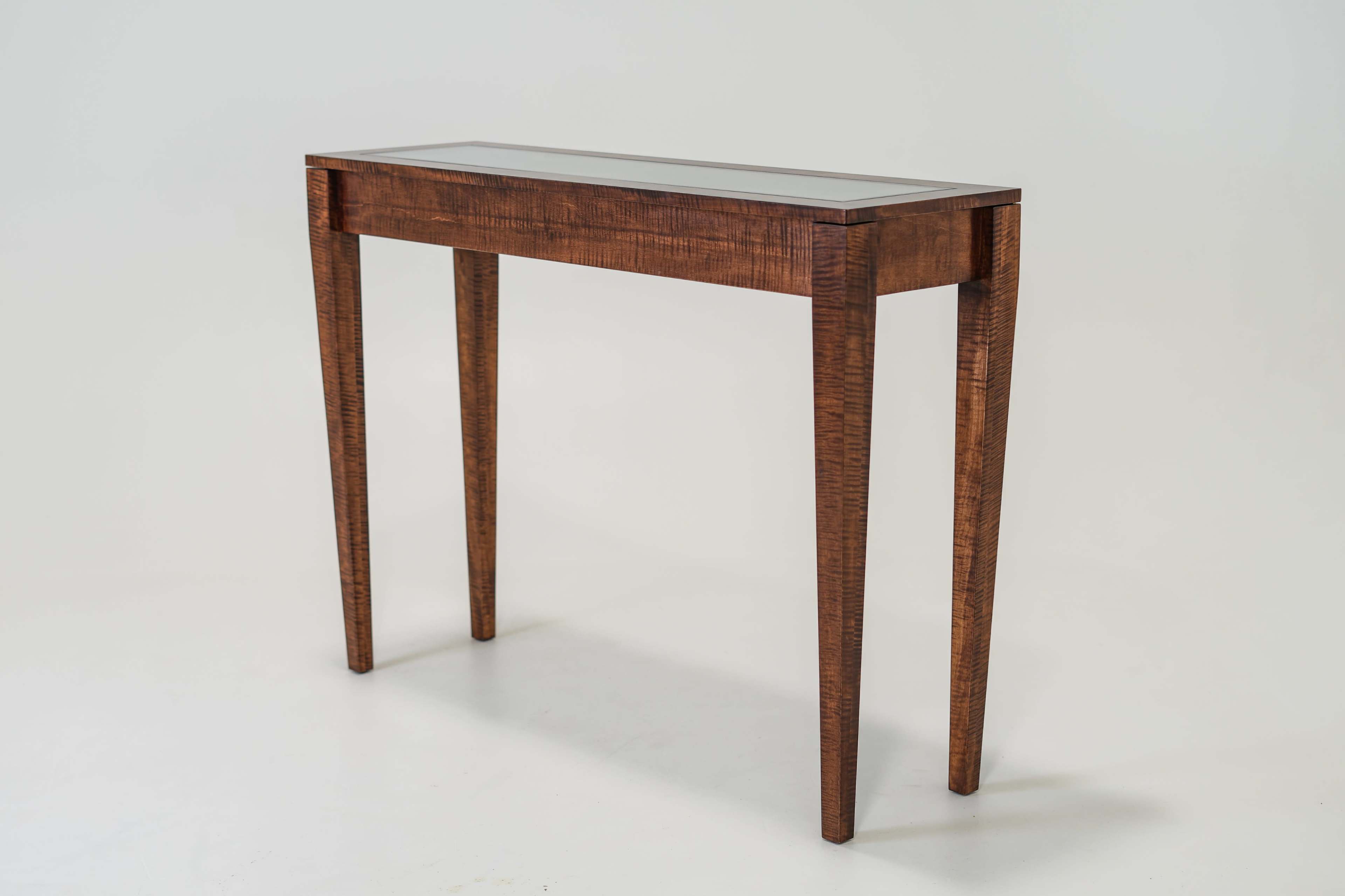 A wooden console table with a glass top and slender legs stands against a light background.