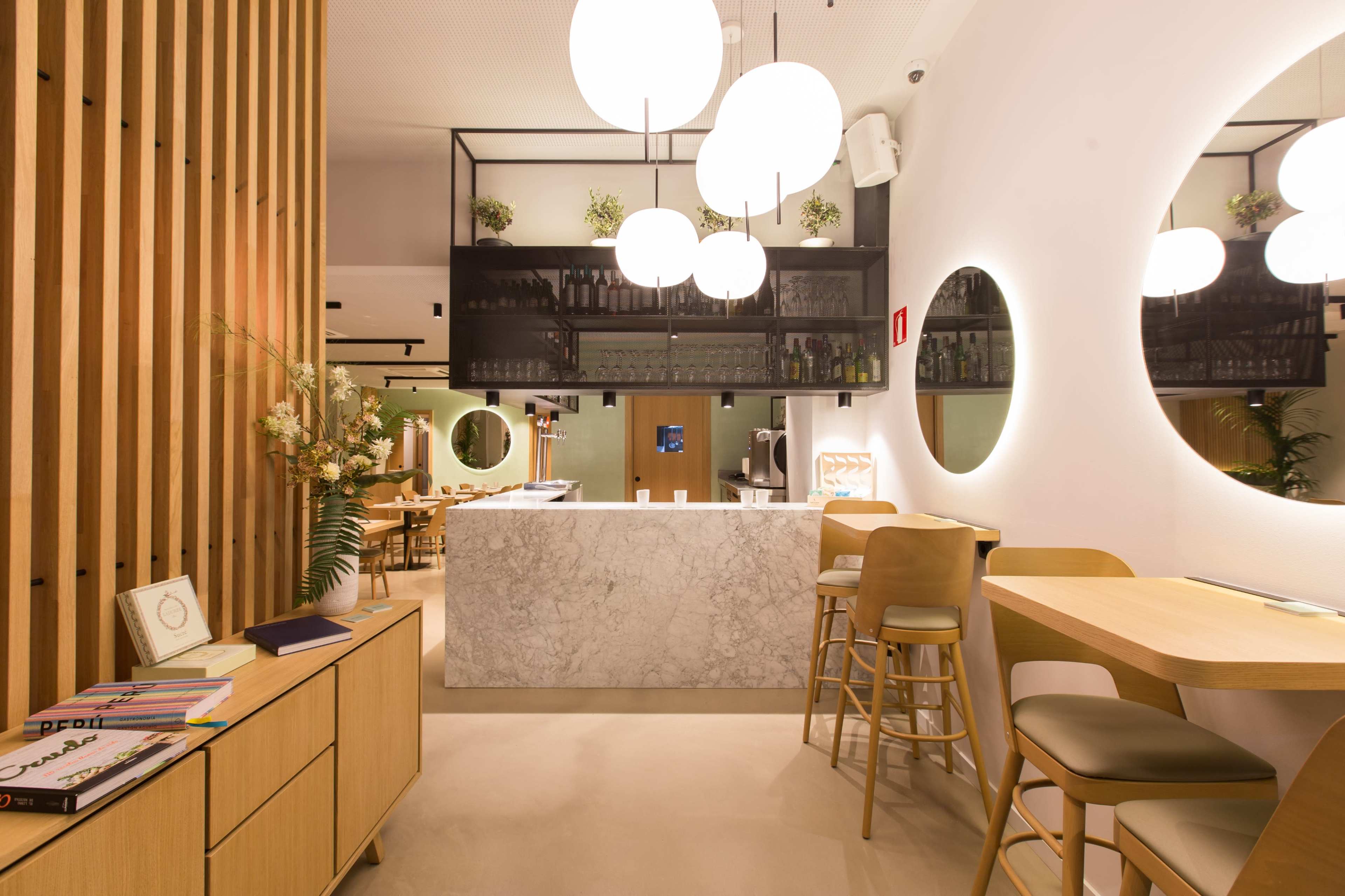 A modern restaurant interior featuring a marble bar, wooden accents, and round mirrors with soft lighting.